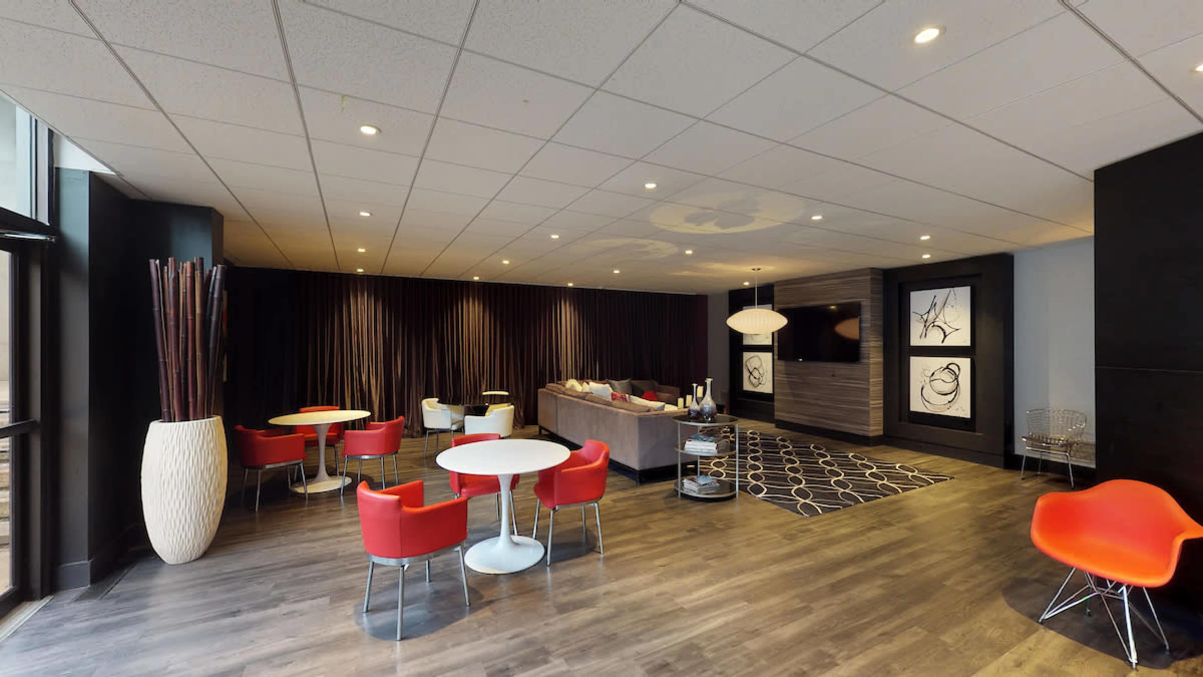 A modern lounge area with red and white furniture, including tables and chairs, alongside a gray sofa and decorative artwork on the walls.