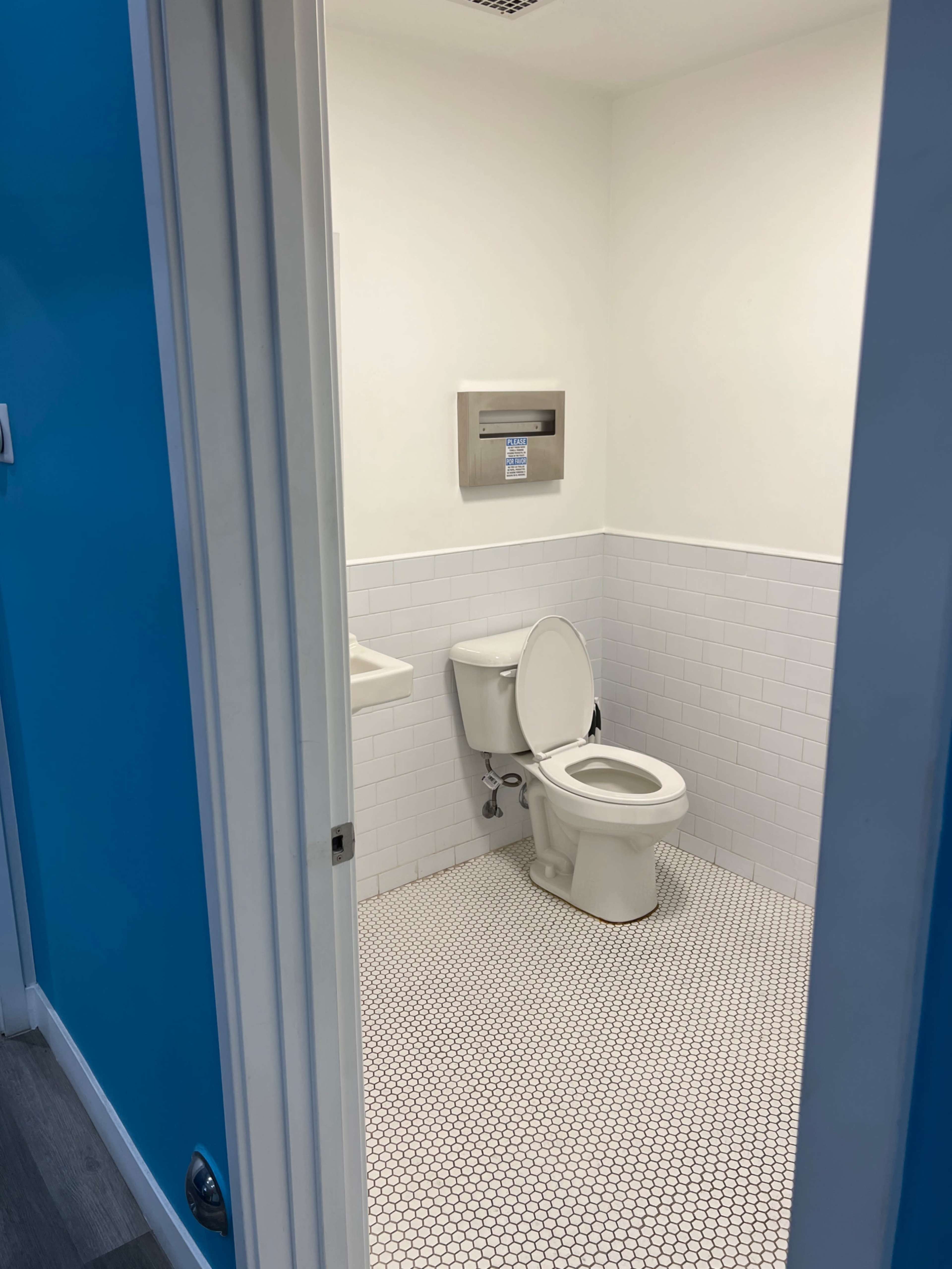 A small, clean bathroom with white tiled walls and a toilet is visible through an open door.