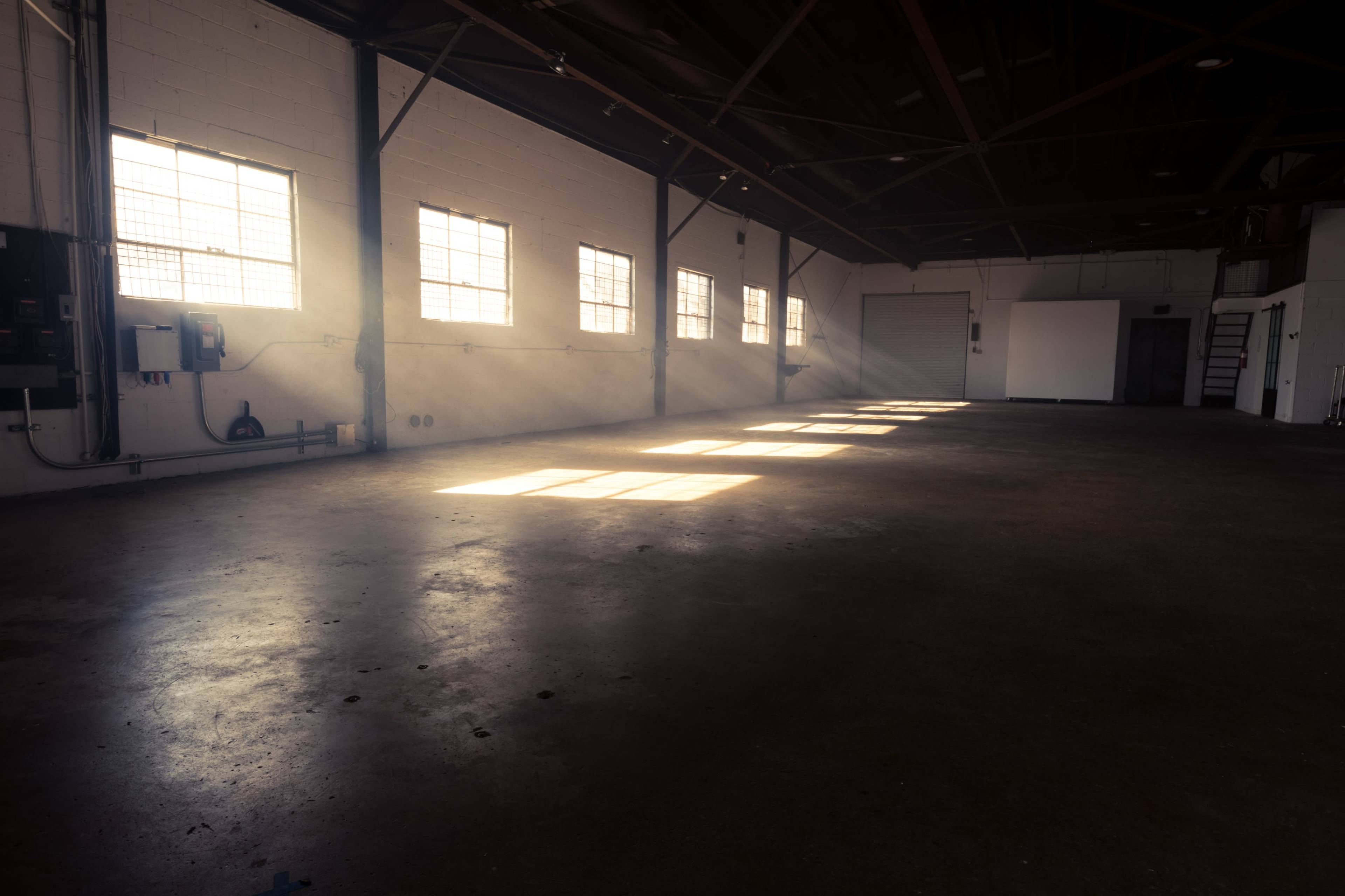 A sunlit industrial space with concrete flooring and large windows casting light beams.