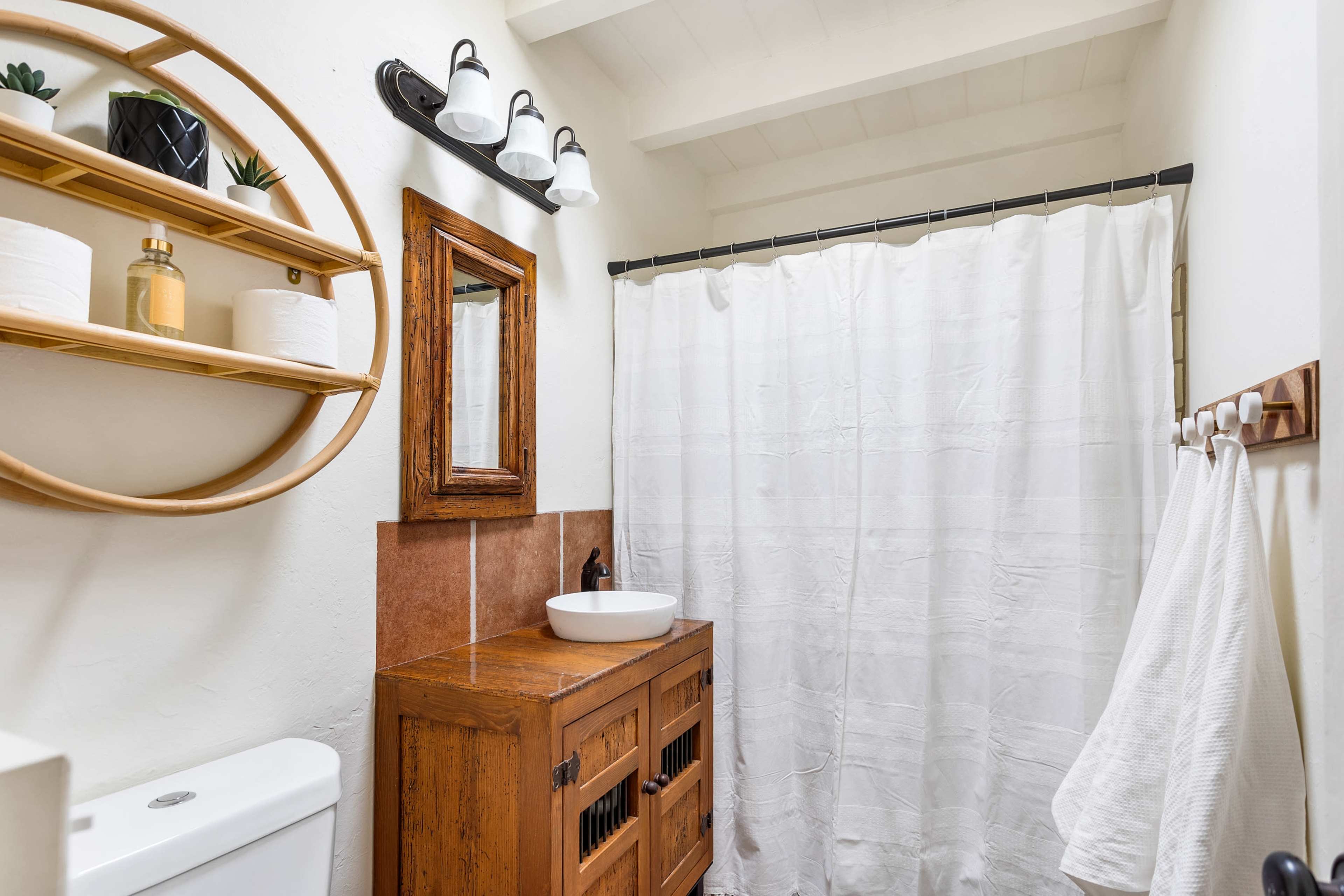 A small bathroom with a wooden cabinet, a round mirror, a white shower curtain, and a light fixture with three bulbs.