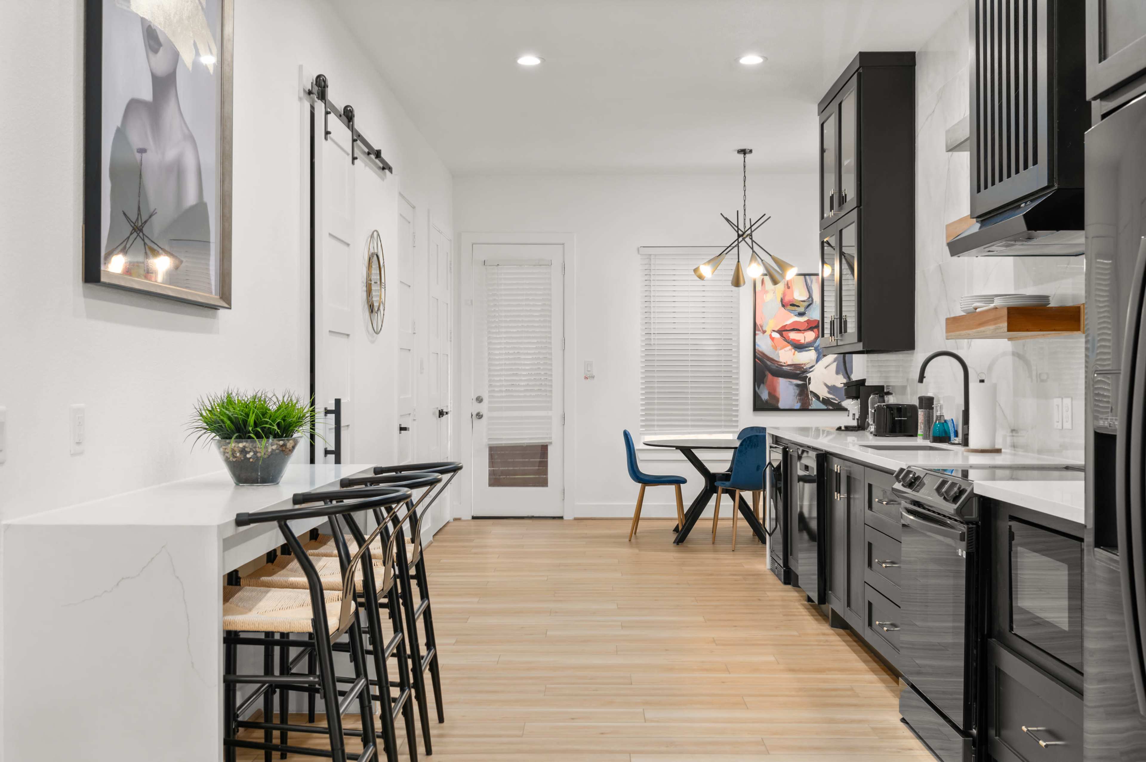 A modern kitchen features black cabinets, stainless steel appliances, a white countertop, and seating at a small table with bar stools.
