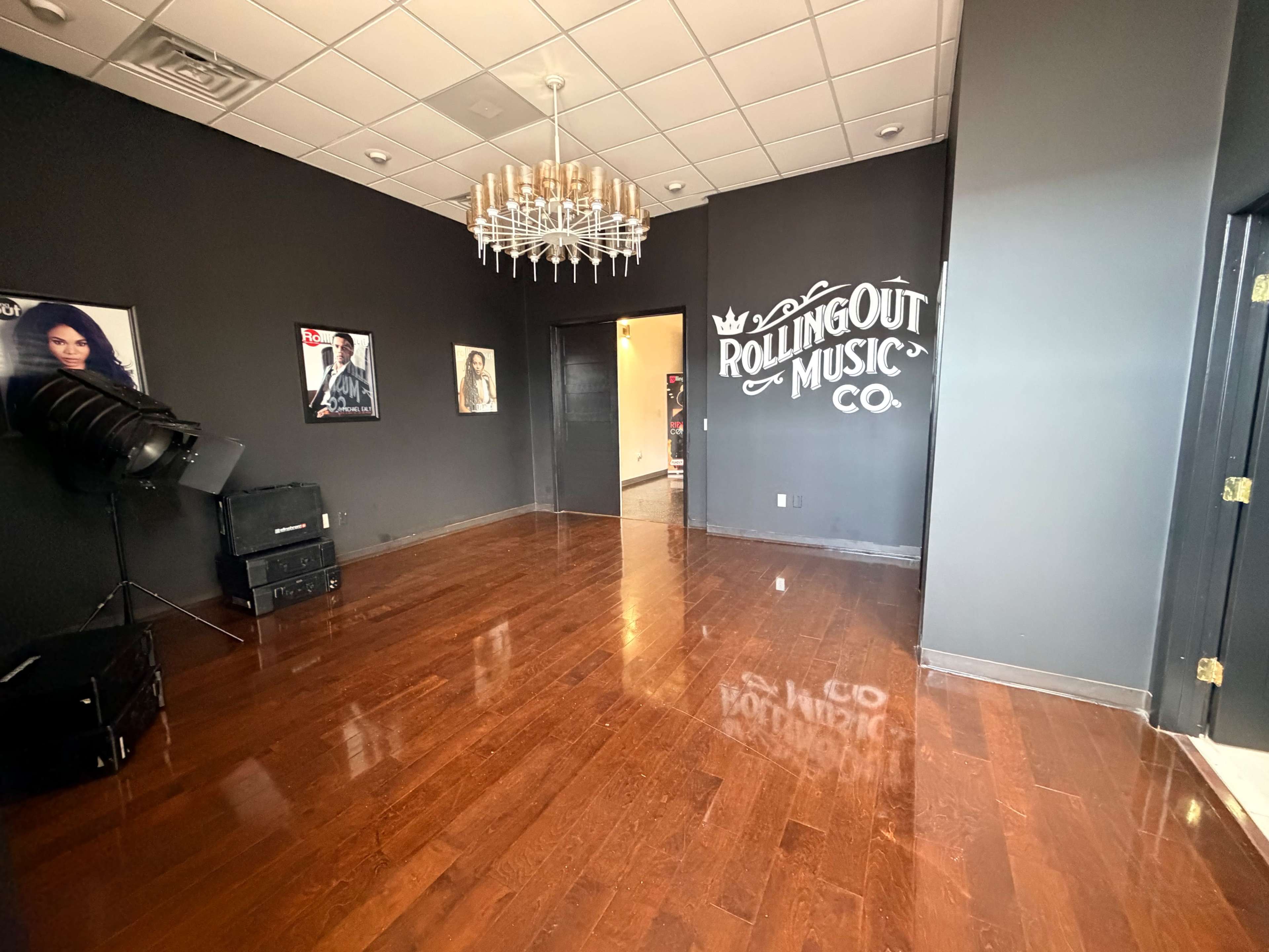 The room features dark walls, polished hardwood floors, and a chandelier, with framed photos and a sign that reads "ROLLINGOUT MUSIC CO." on one wall.