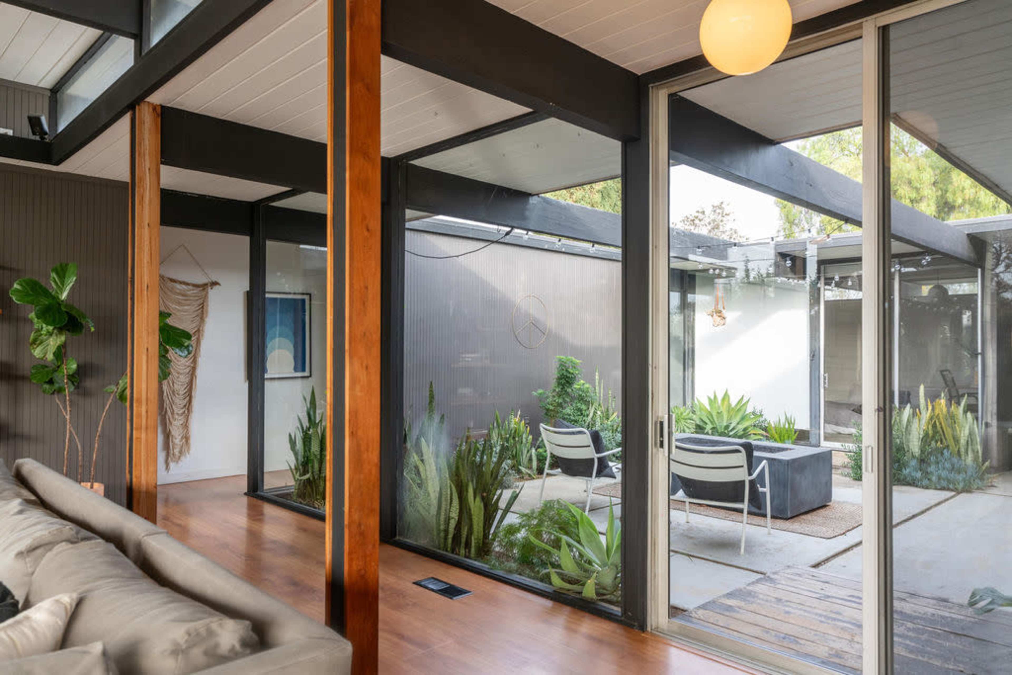 The image shows a modern living space with large glass doors that open to an enclosed patio featuring seating and various plants.