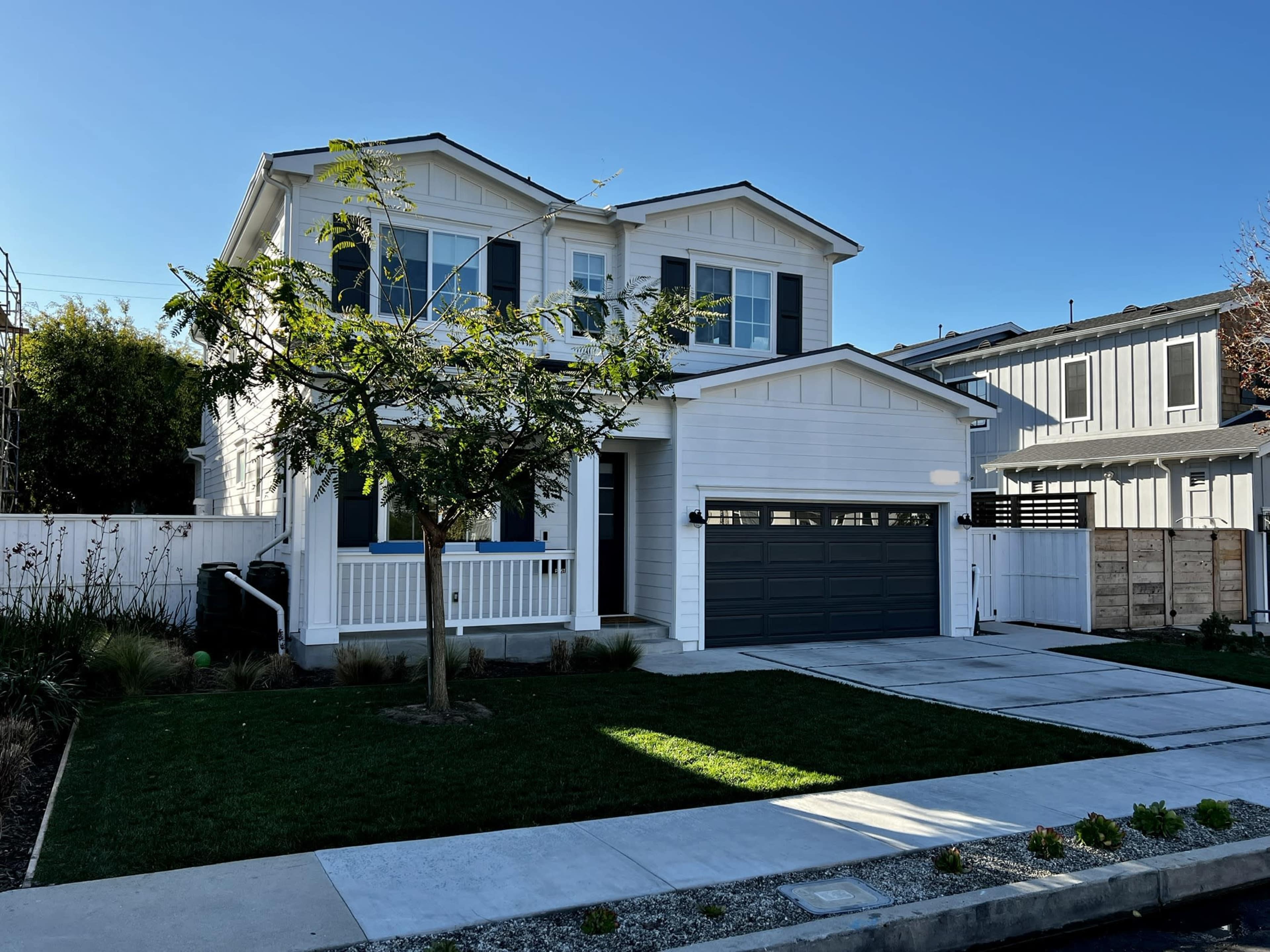 A two-story white house with black shutters and a gray garage door is situated on a landscaped corner lot.