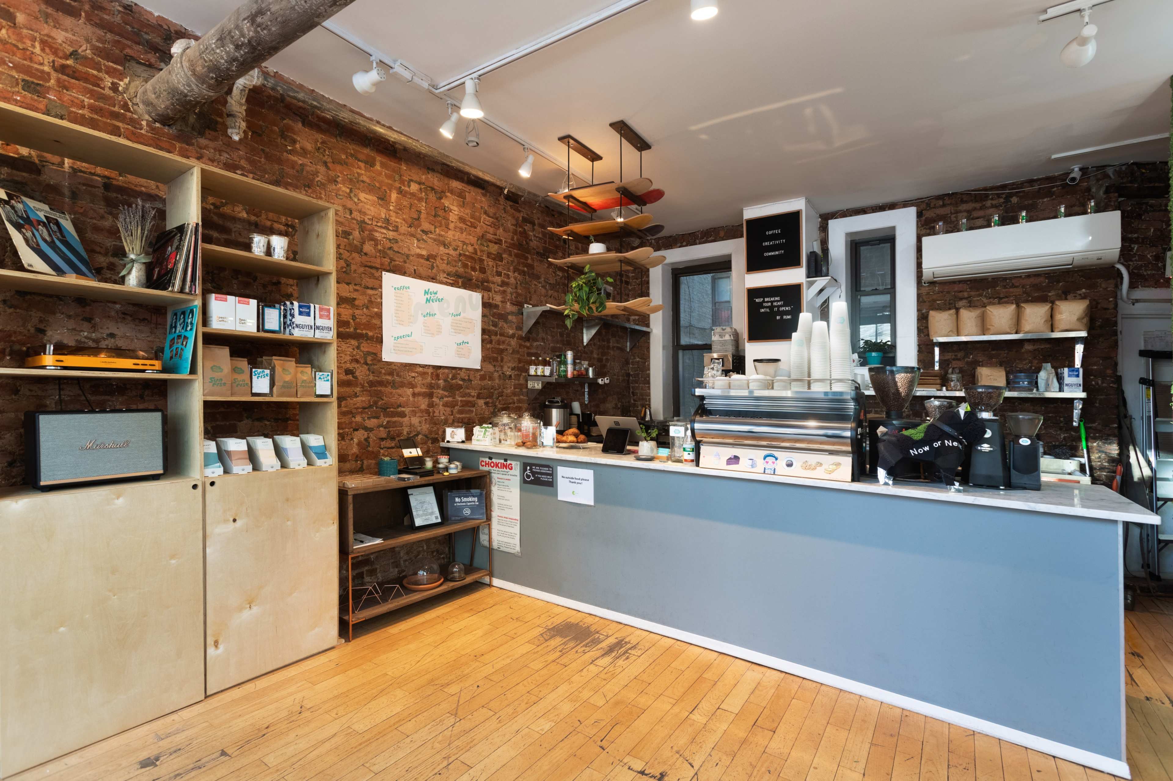 A modern coffee shop interior with exposed brick walls, a wooden floor, and a counter displaying coffee equipment and various products.