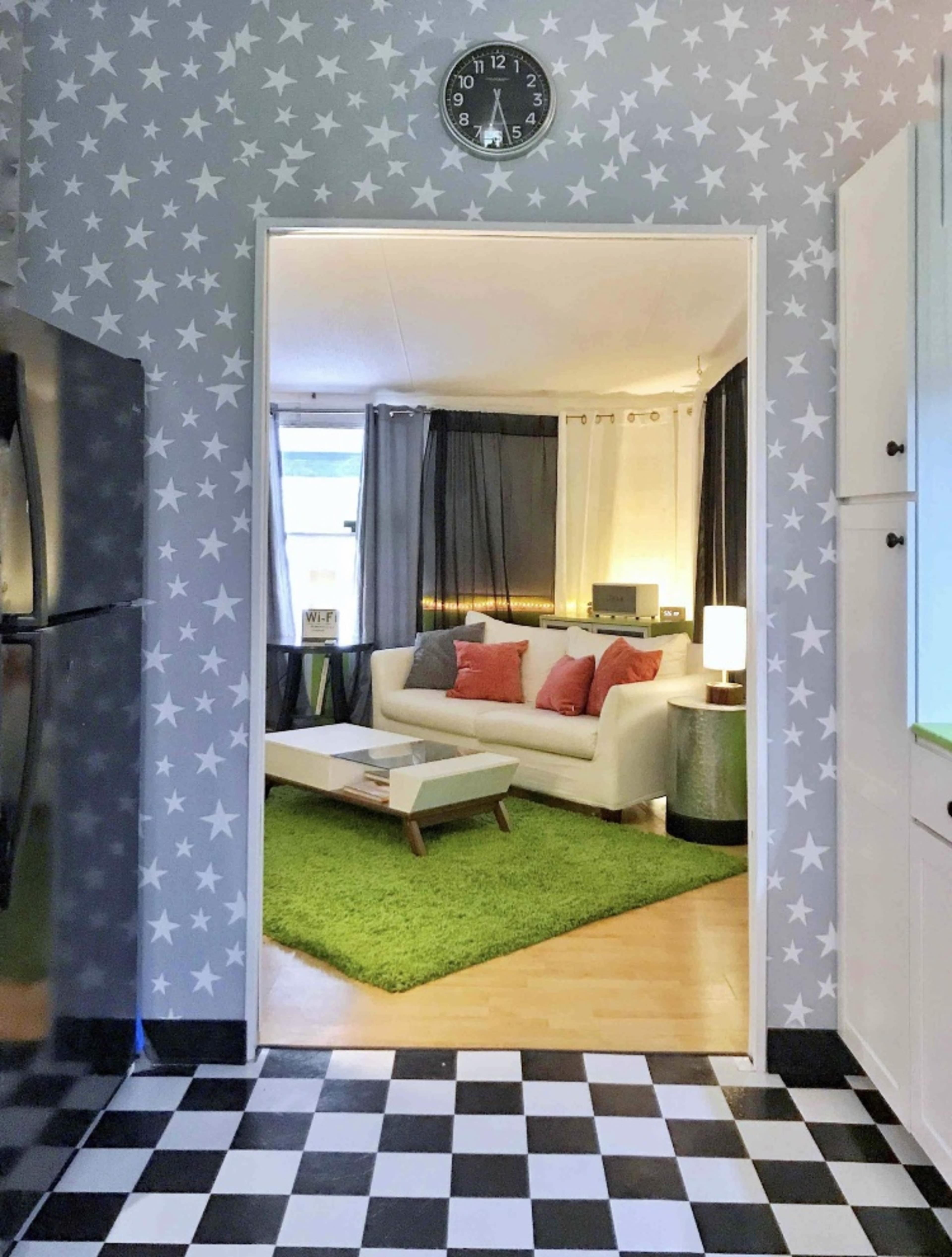 A view from a kitchen into a living room featuring a white sofa, green rug, and a star-patterned wall.