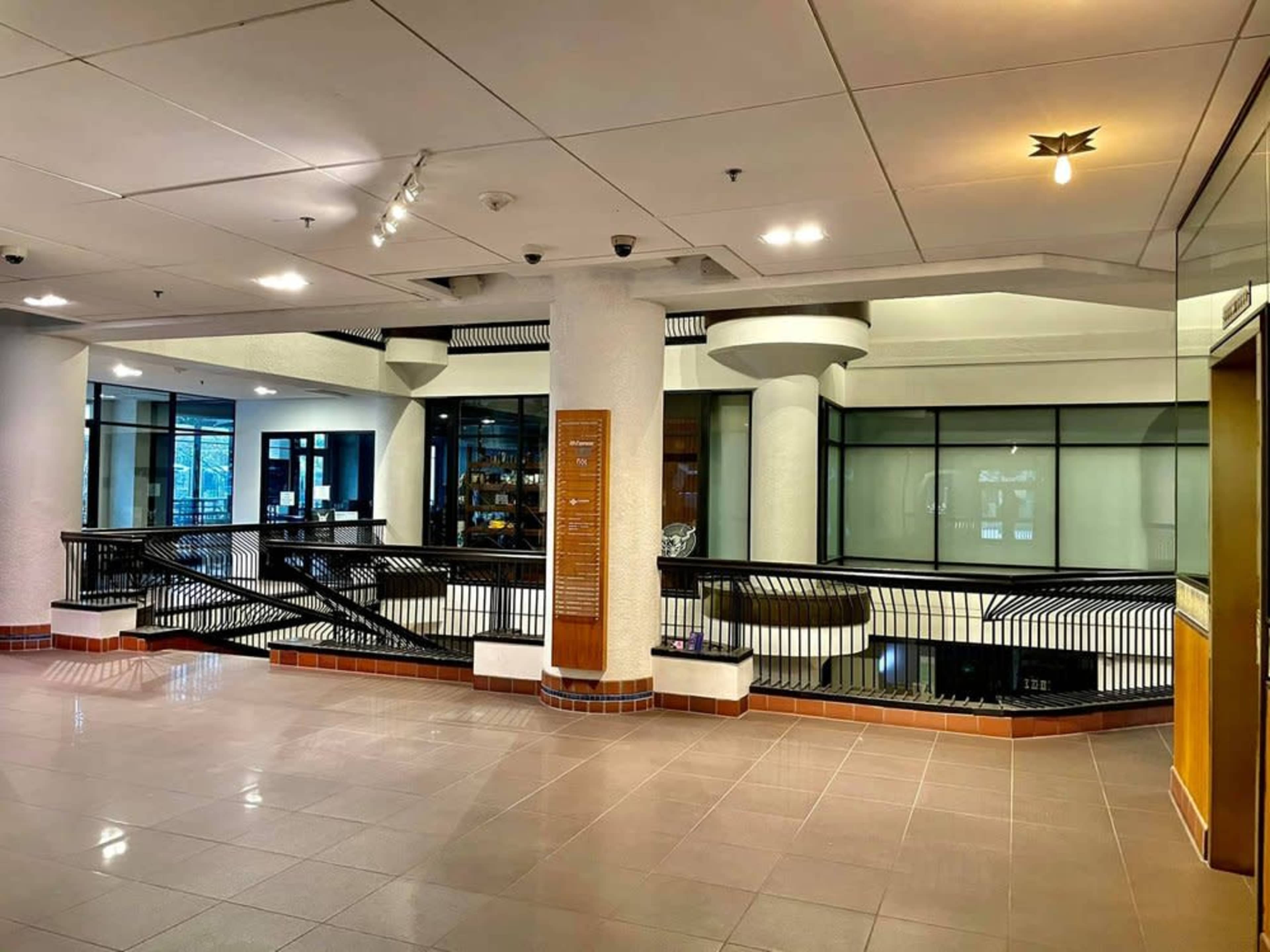 The image shows a modern indoor space with large windows, a multi-level layout, and a sleek railing.