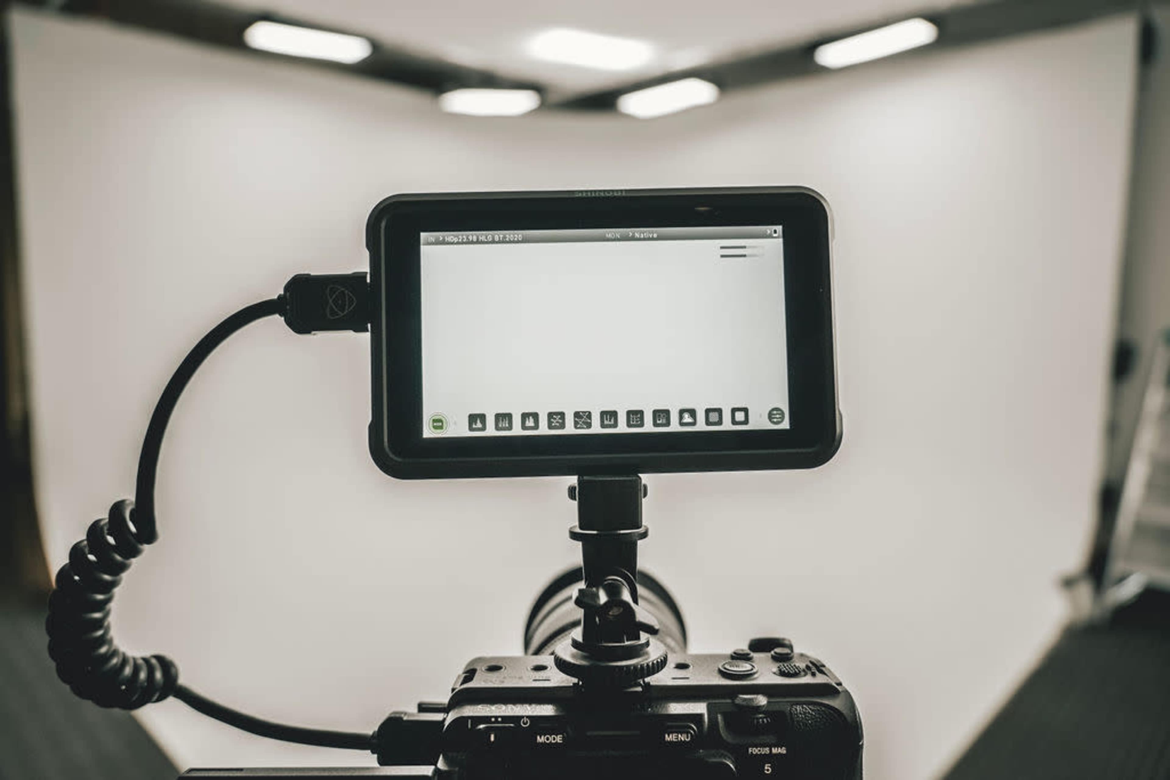 A camera is positioned in front of a plain white backdrop, displaying a screen with various icons and options.