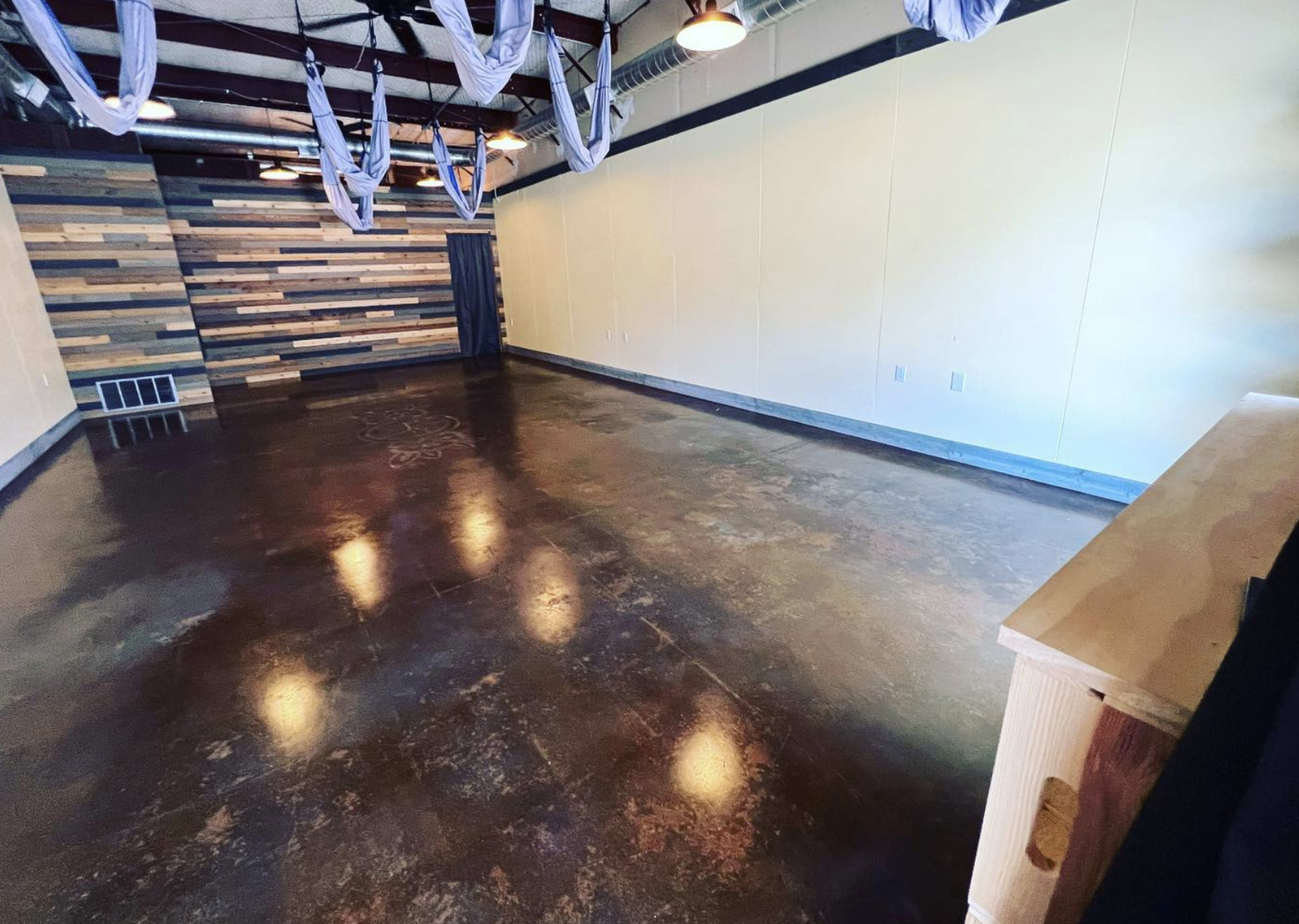 An empty room with a polished concrete floor, wooden accent wall, and suspended fabric setup for aerial activities.
