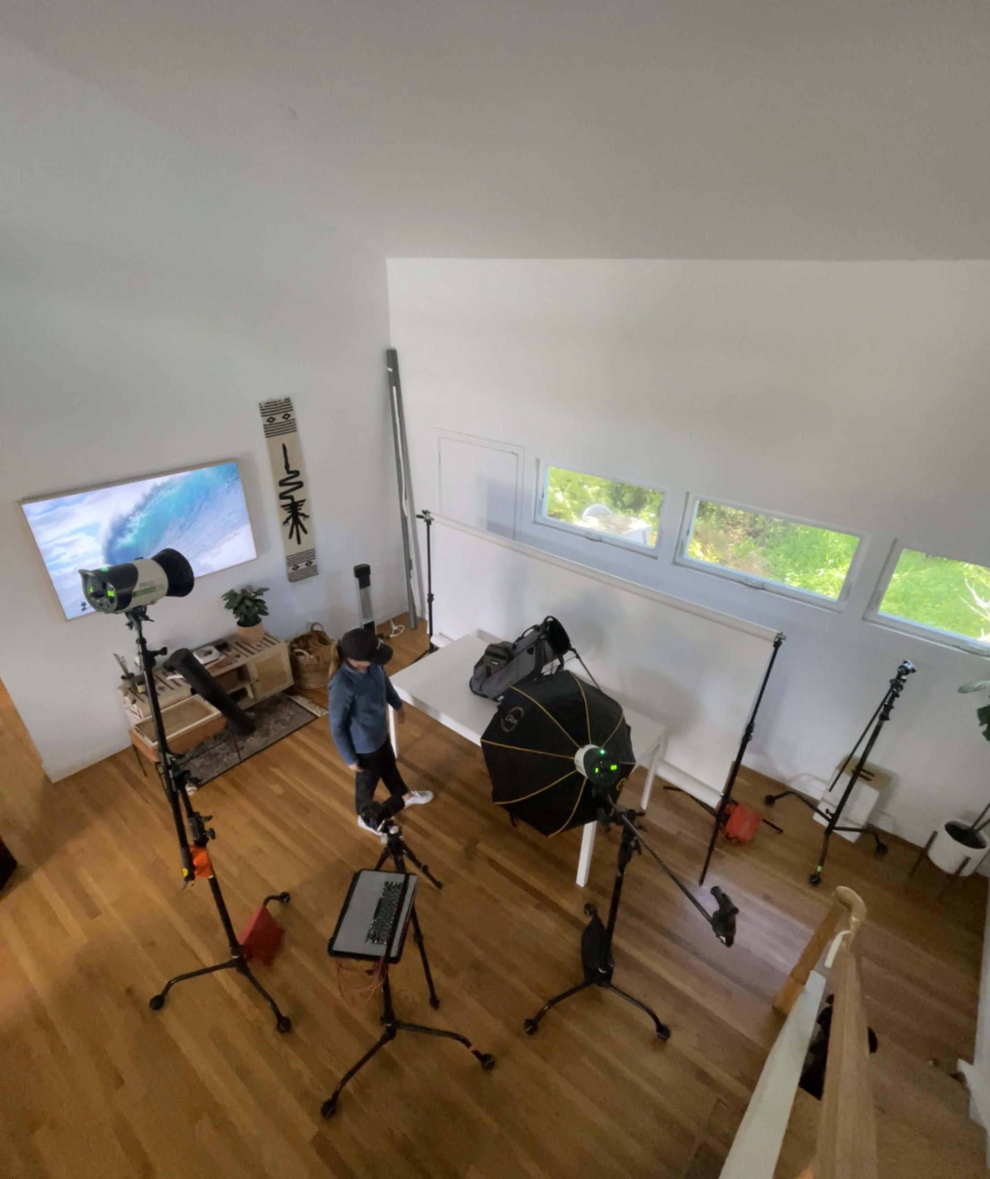 A person stands in a well-lit room filled with photography equipment, including tripods, a backdrop, and studio lights.