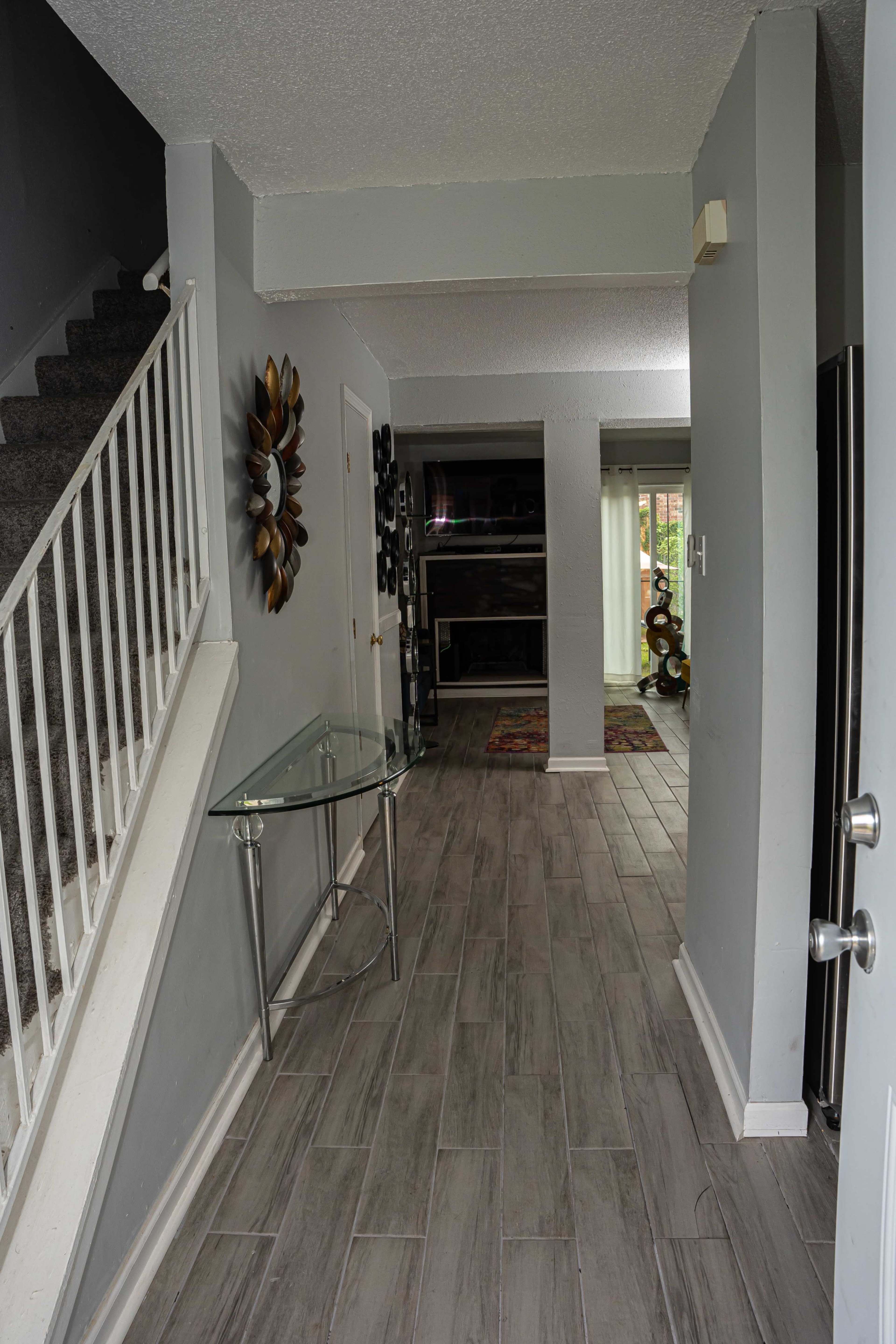 A hallway with a glass table and a staircase on one side, leading to a living area in the background.