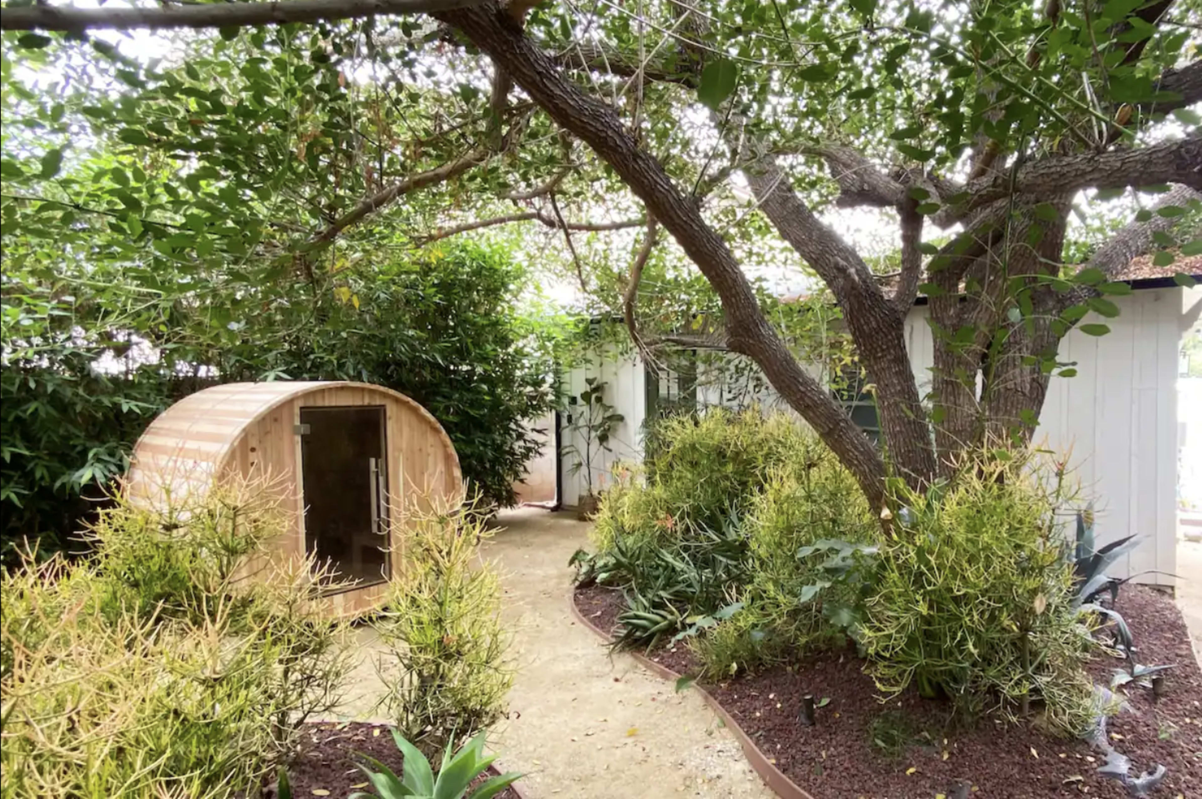 A winding pathway leading past a curved wooden structure and surrounded by lush greenery and trees.