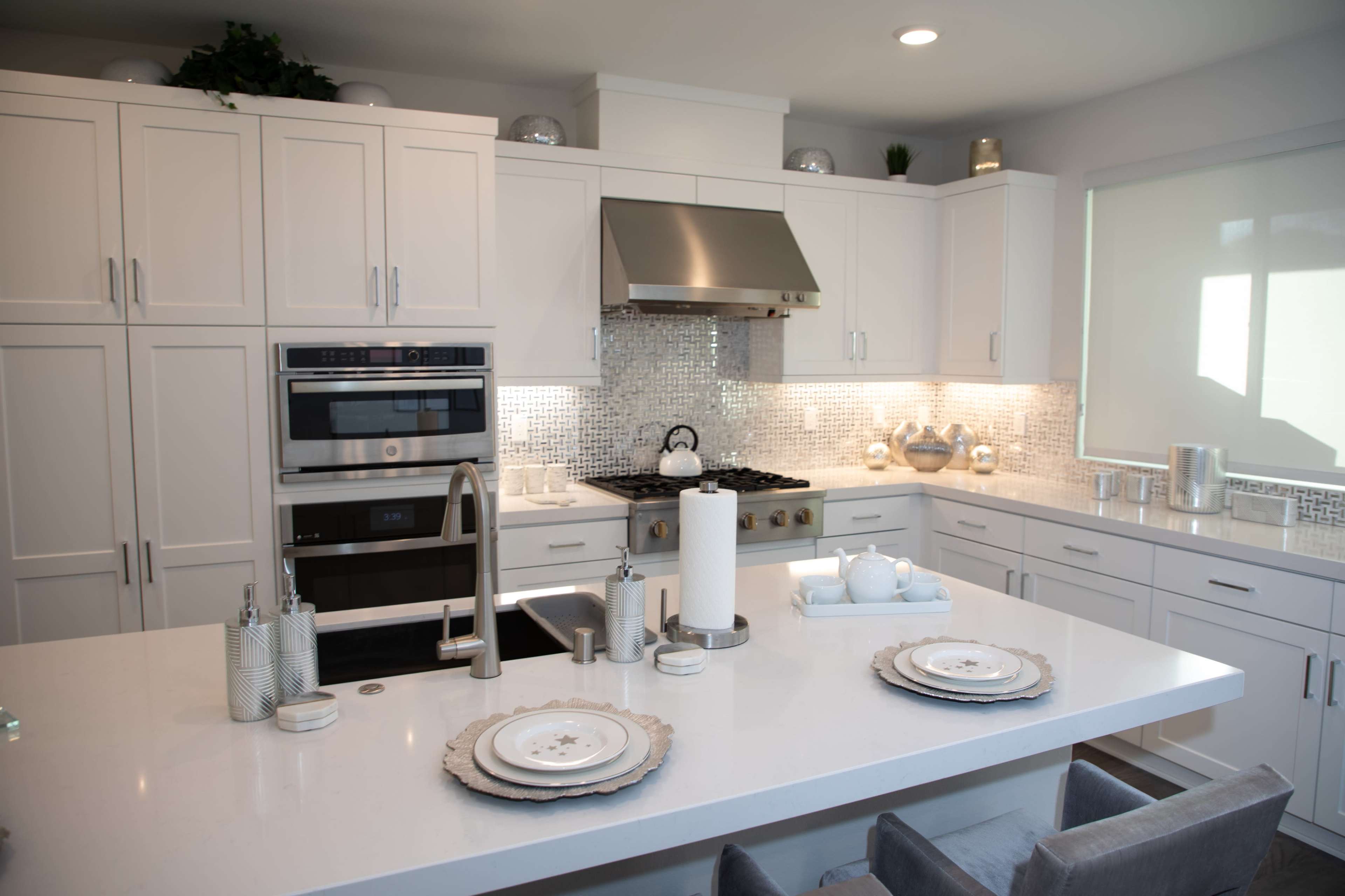 A modern kitchen features white cabinetry, stainless steel appliances, and a central island set with decorative plates and utensils.