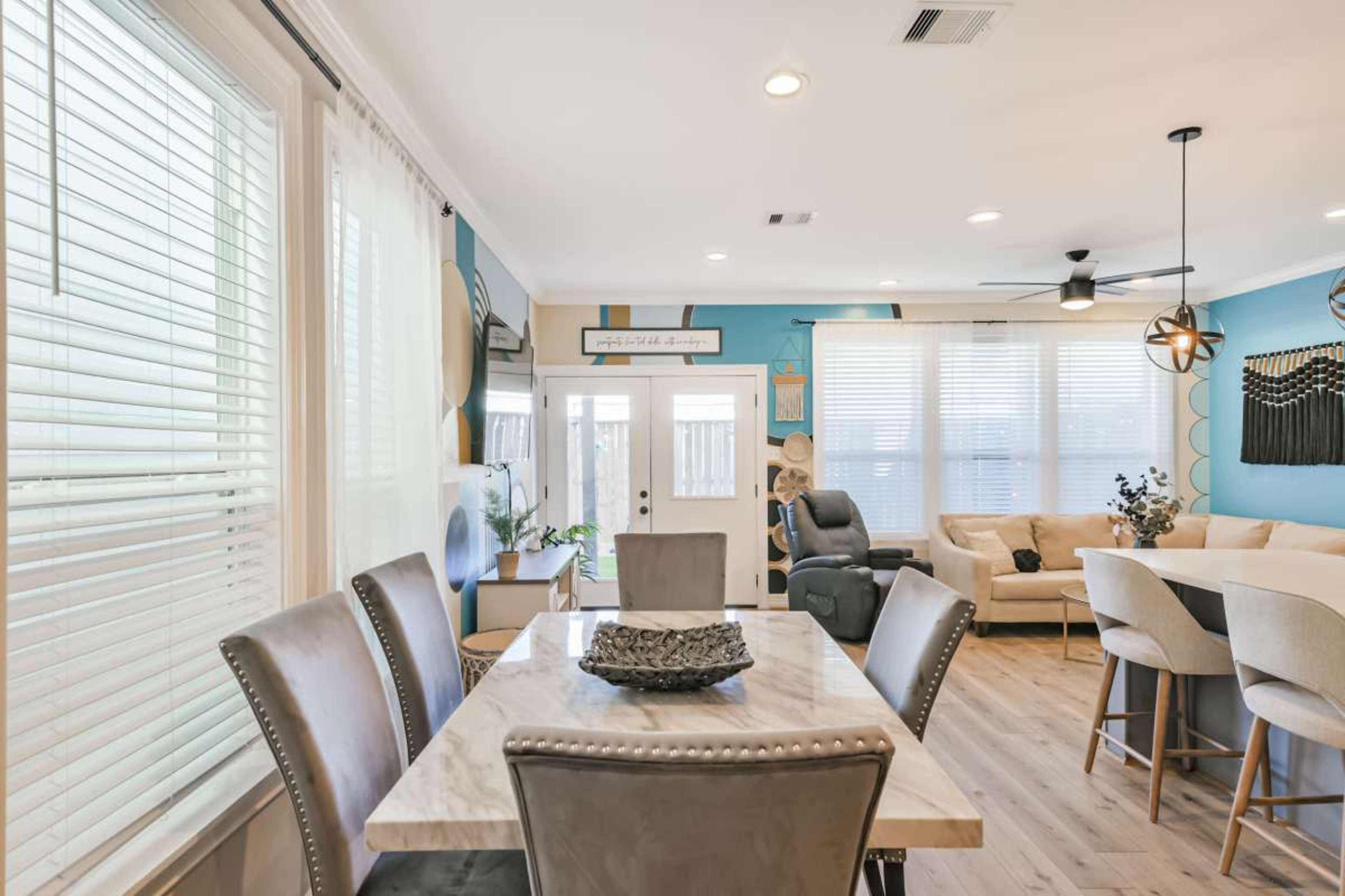 The image shows a modern dining and living area featuring a marble dining table, beige upholstered chairs, and a cozy seating arrangement with a sectional sofa.