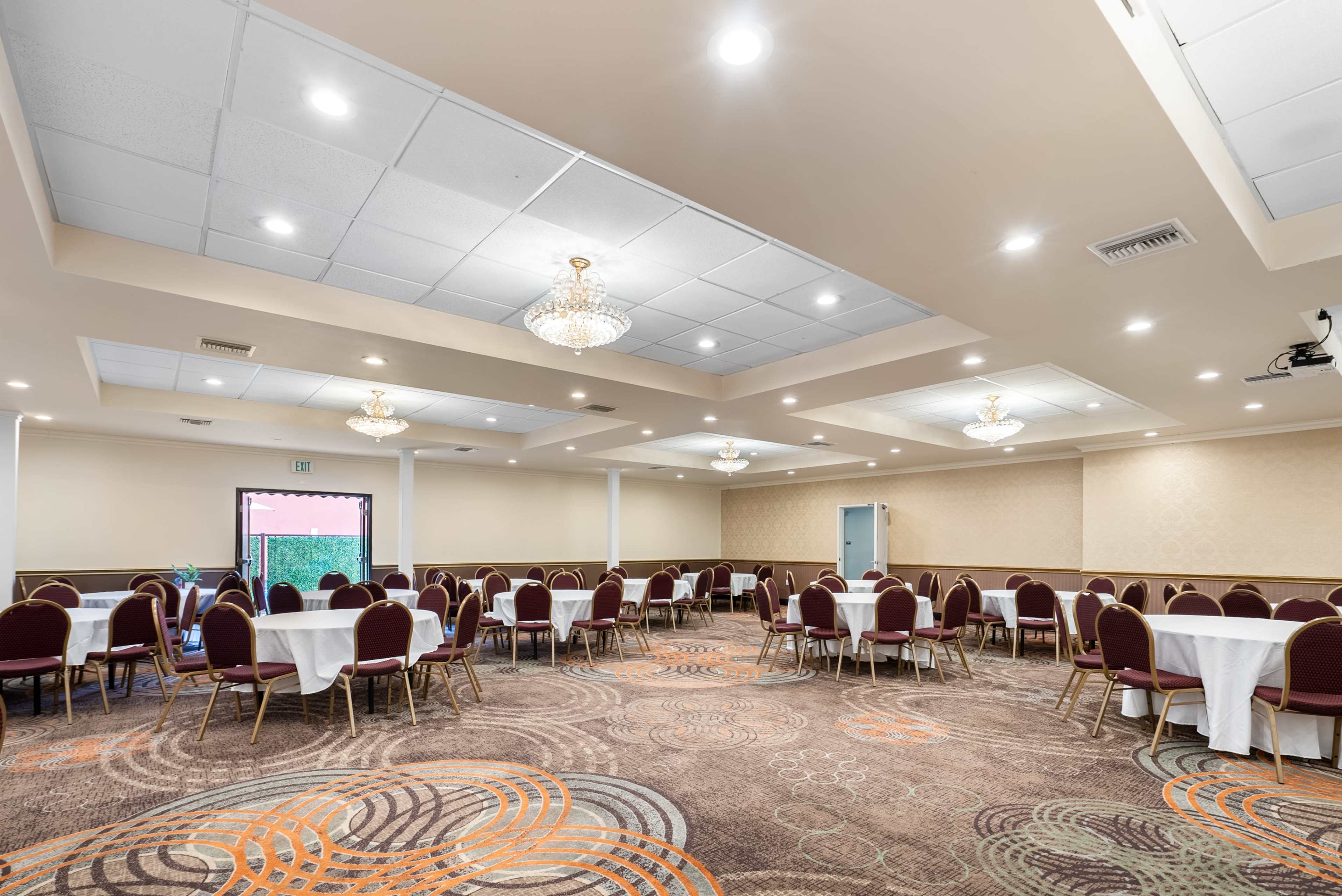 A spacious banquet room set with round tables and chairs, featuring chandeliers and a patterned carpet.