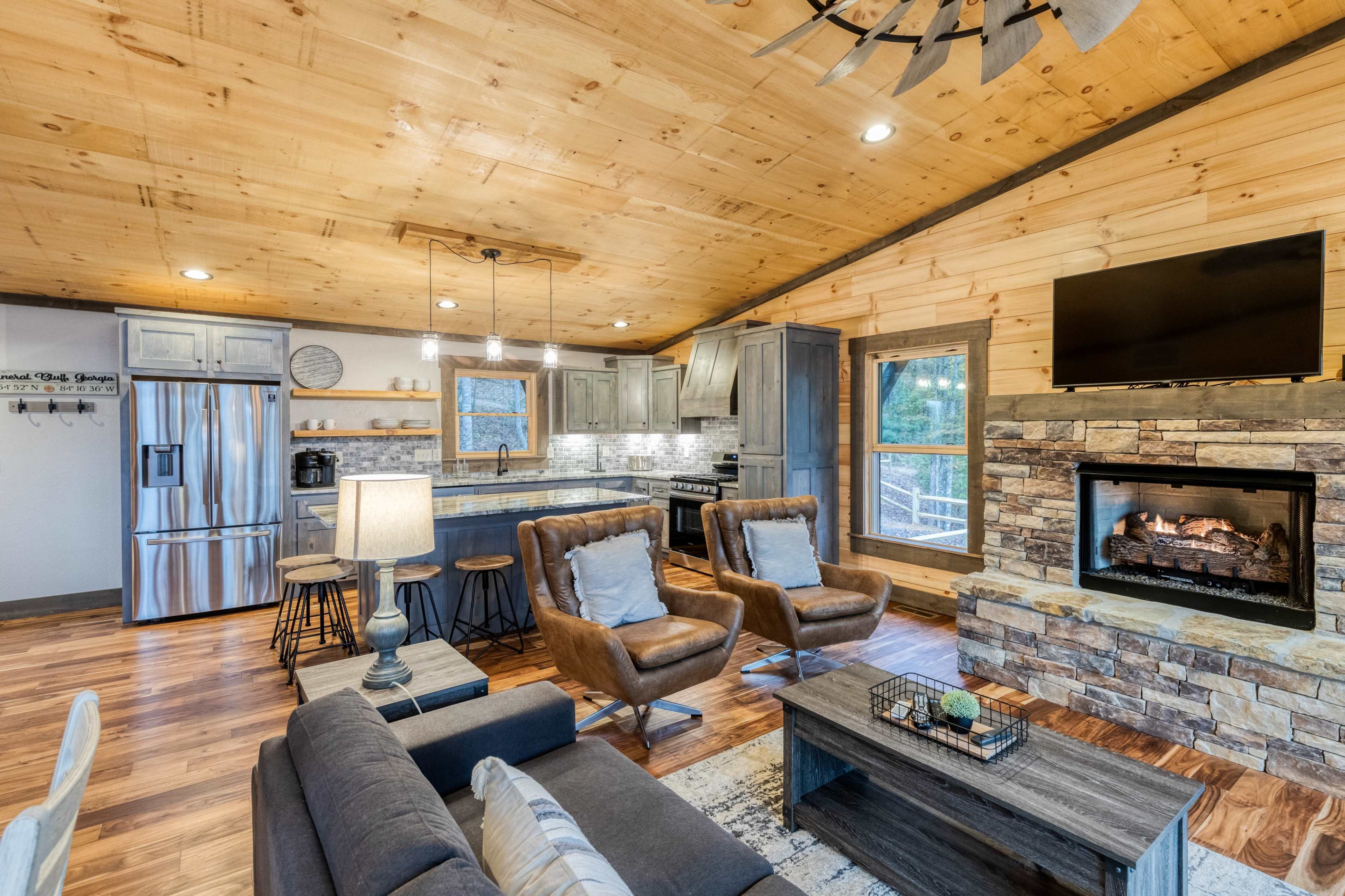 A spacious cabin interior features a modern kitchen, comfortable seating area, and a stone fireplace.