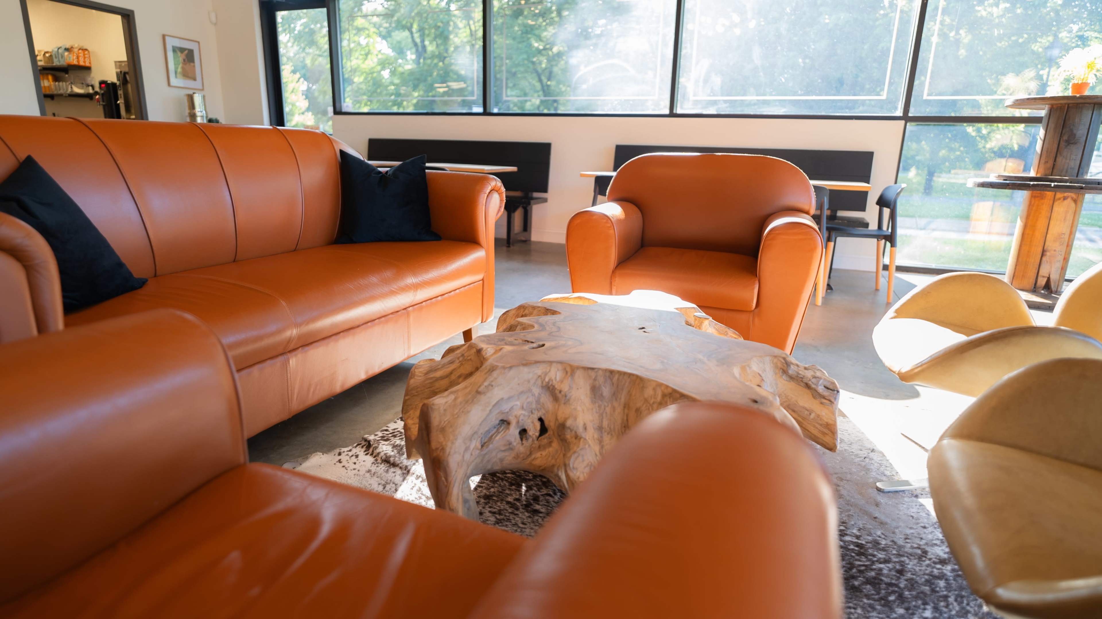 The image shows a cozy seating area with orange leather sofas and a wooden coffee table surrounded by natural light from large windows.