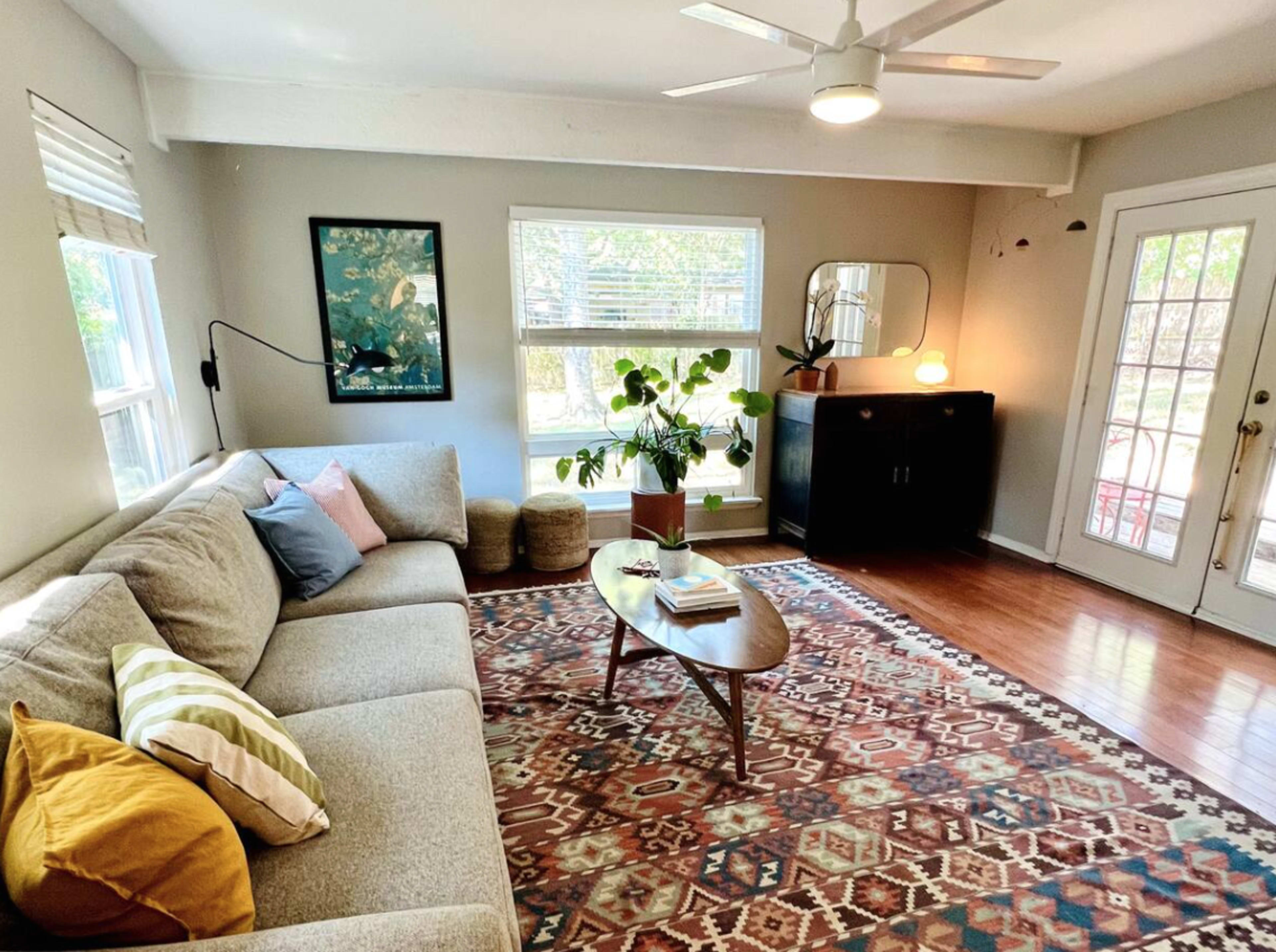 A modern living room features a sofa, a coffee table, a small plant, and large windows that let in natural light.