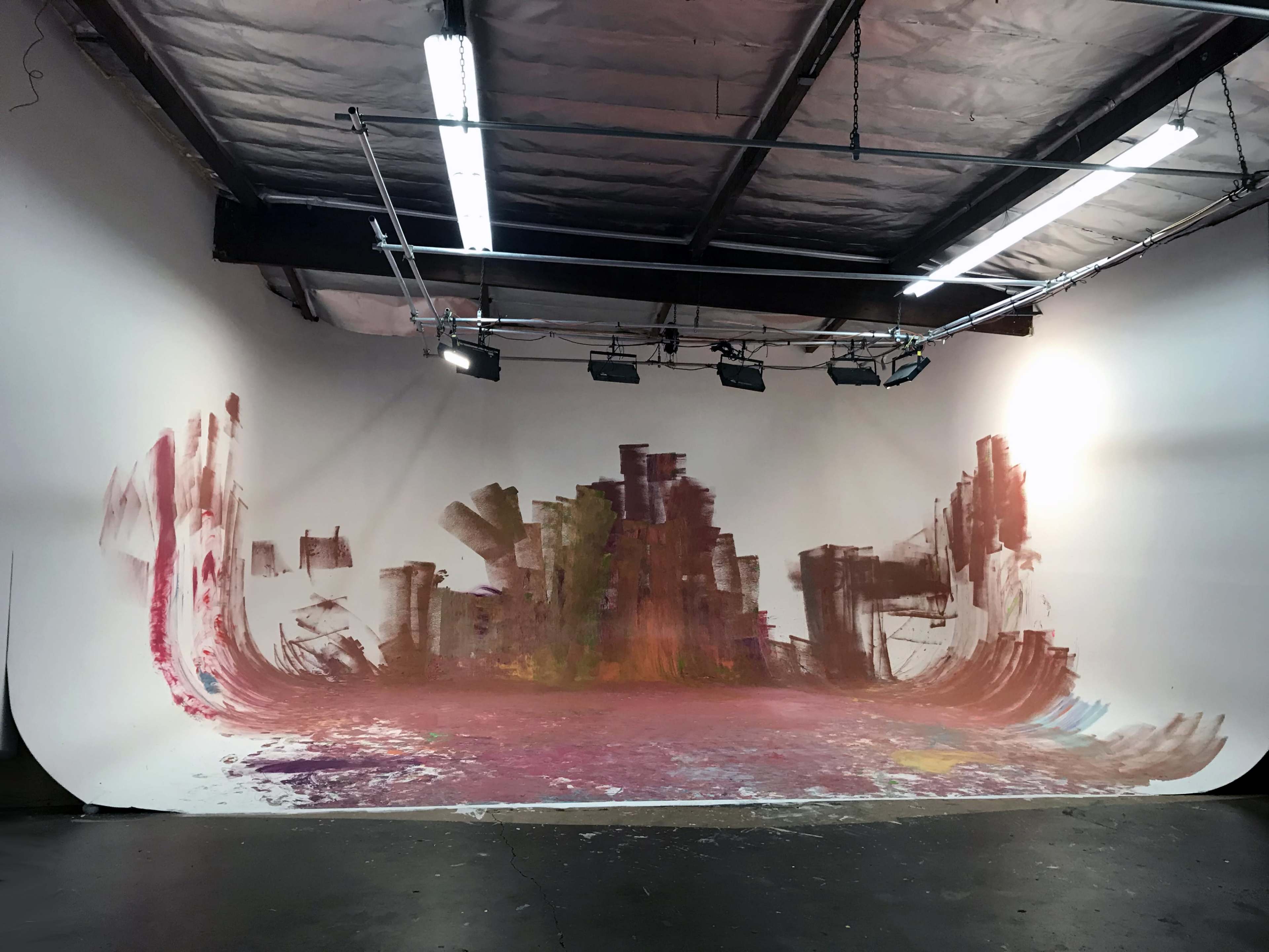 An art studio with a large white backdrop featuring bold, abstract paint strokes in various colors.