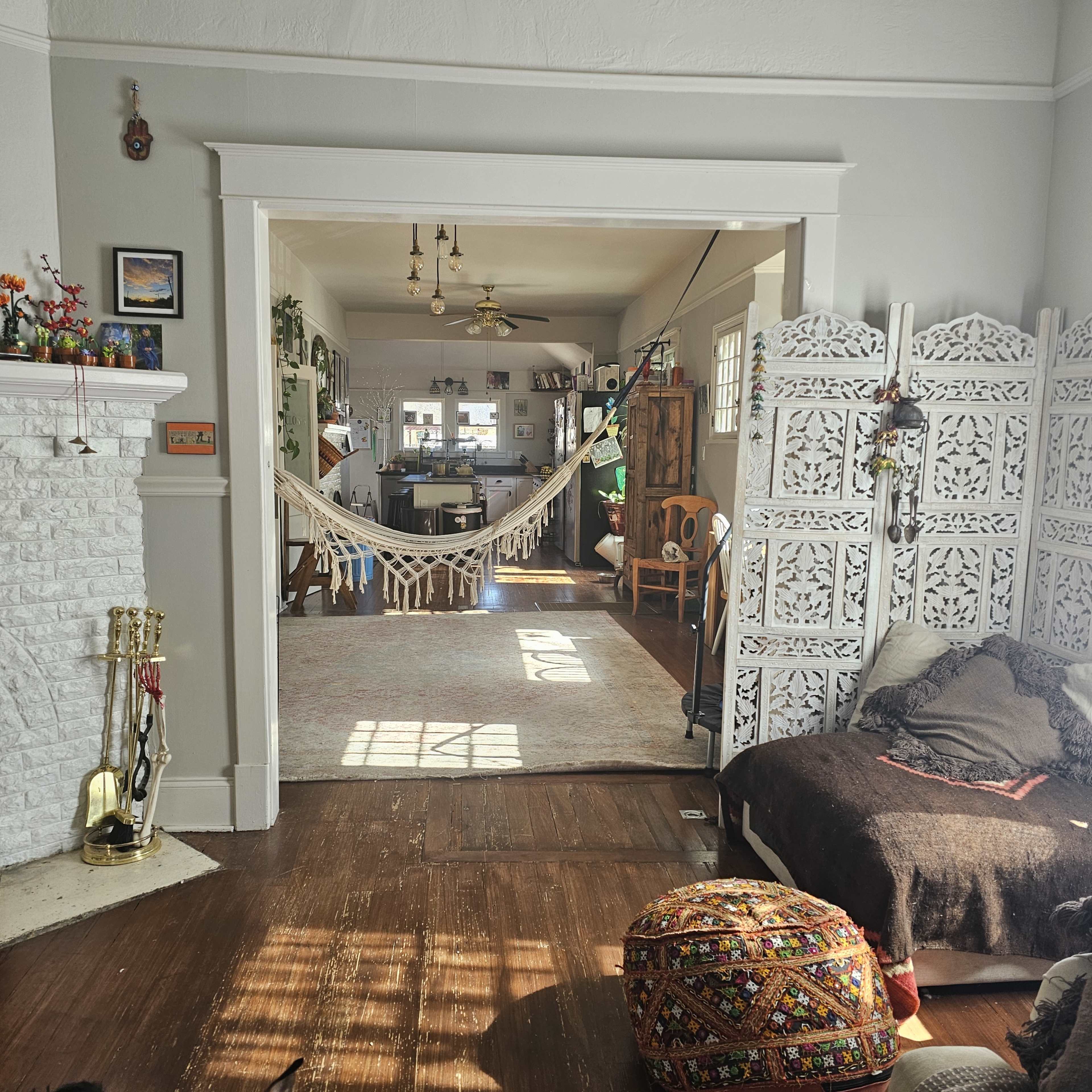 A cozy living room features a hammock draped between two walls, with a large decorative screen and various furniture pieces visible in the background.