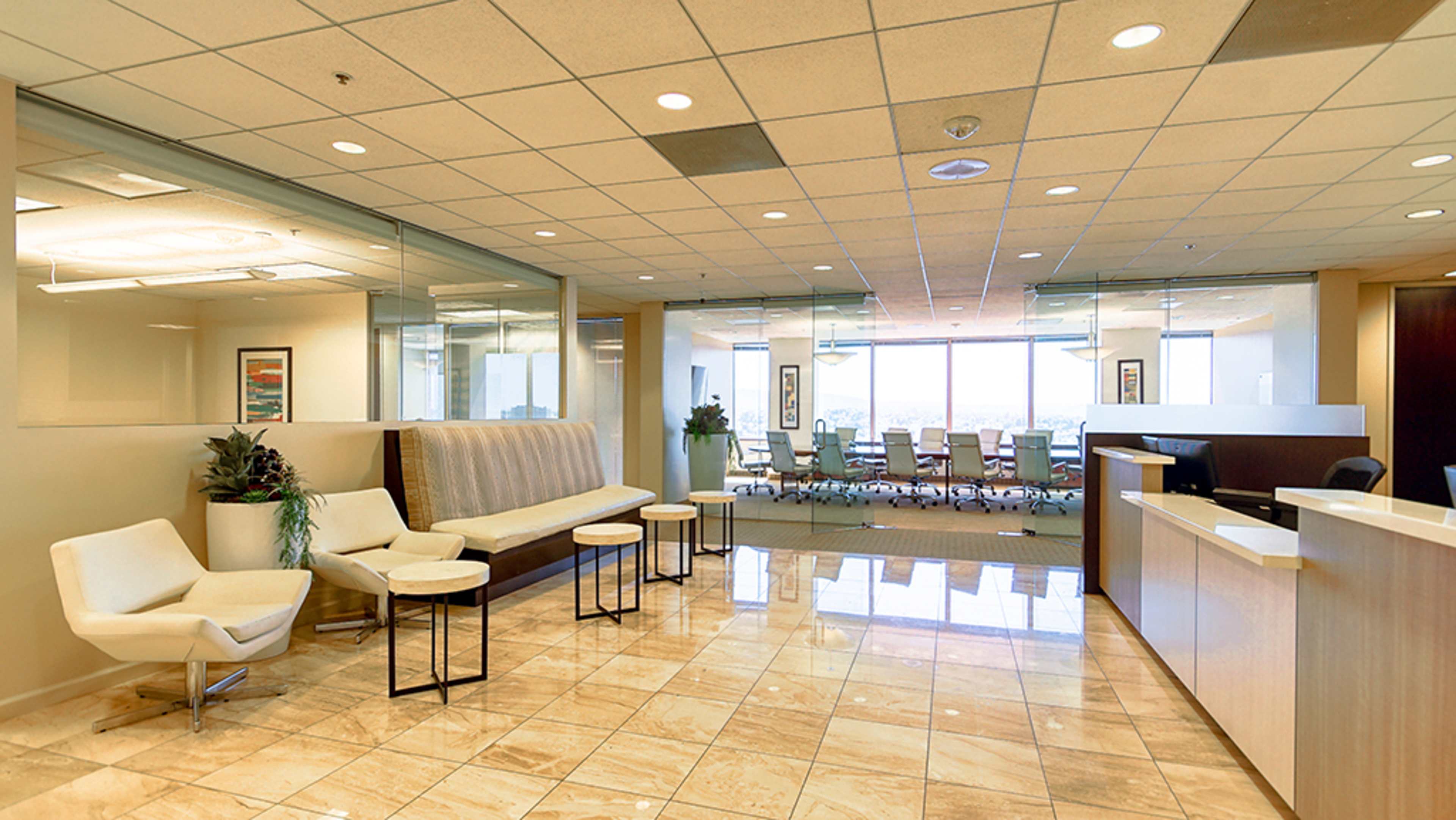 The image shows a modern office reception area with seating, a reception desk, and a conference room visible in the background.