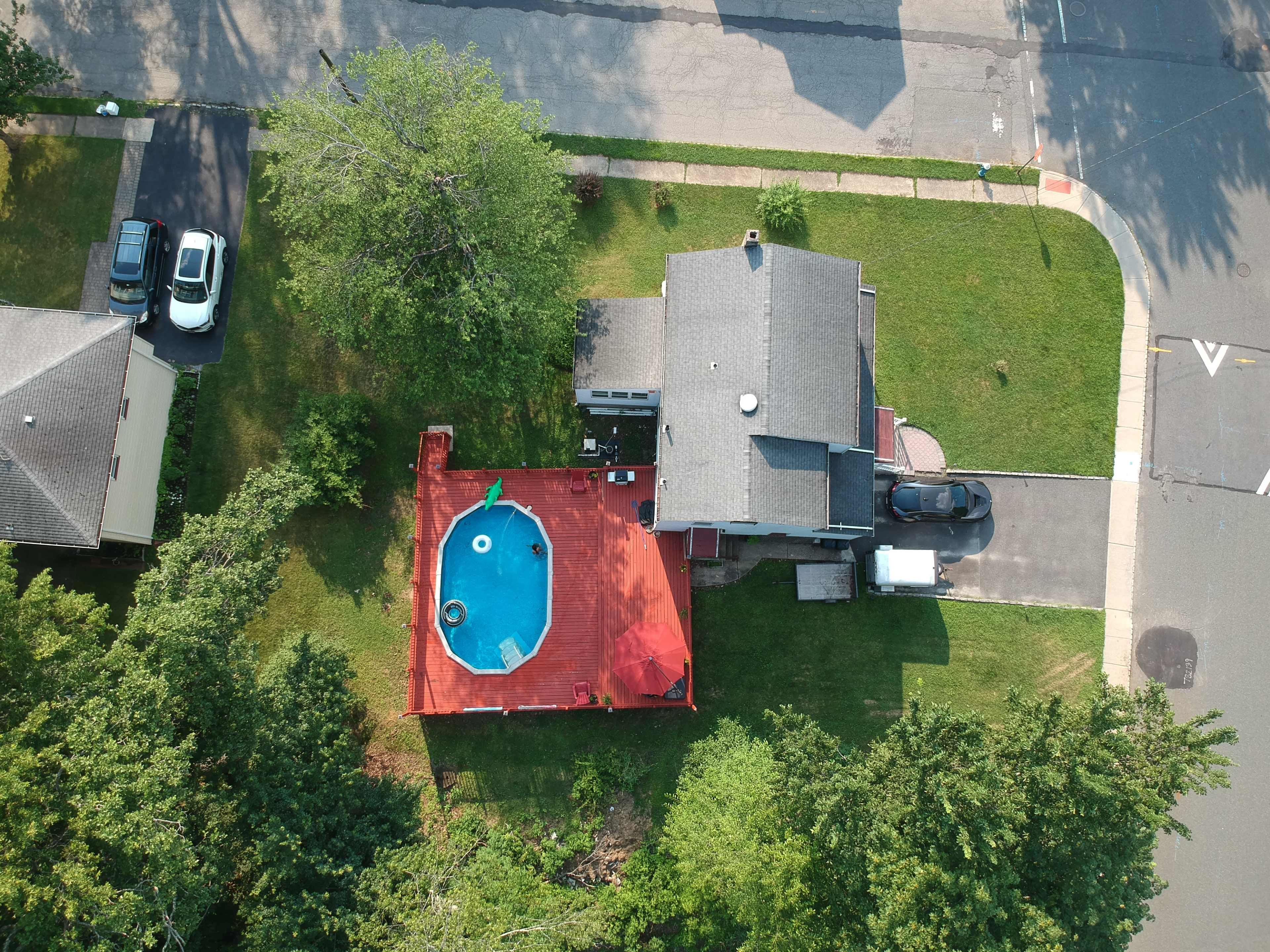 The image shows an aerial view of a house with a red deck and a swimming pool in the backyard, surrounded by greenery.