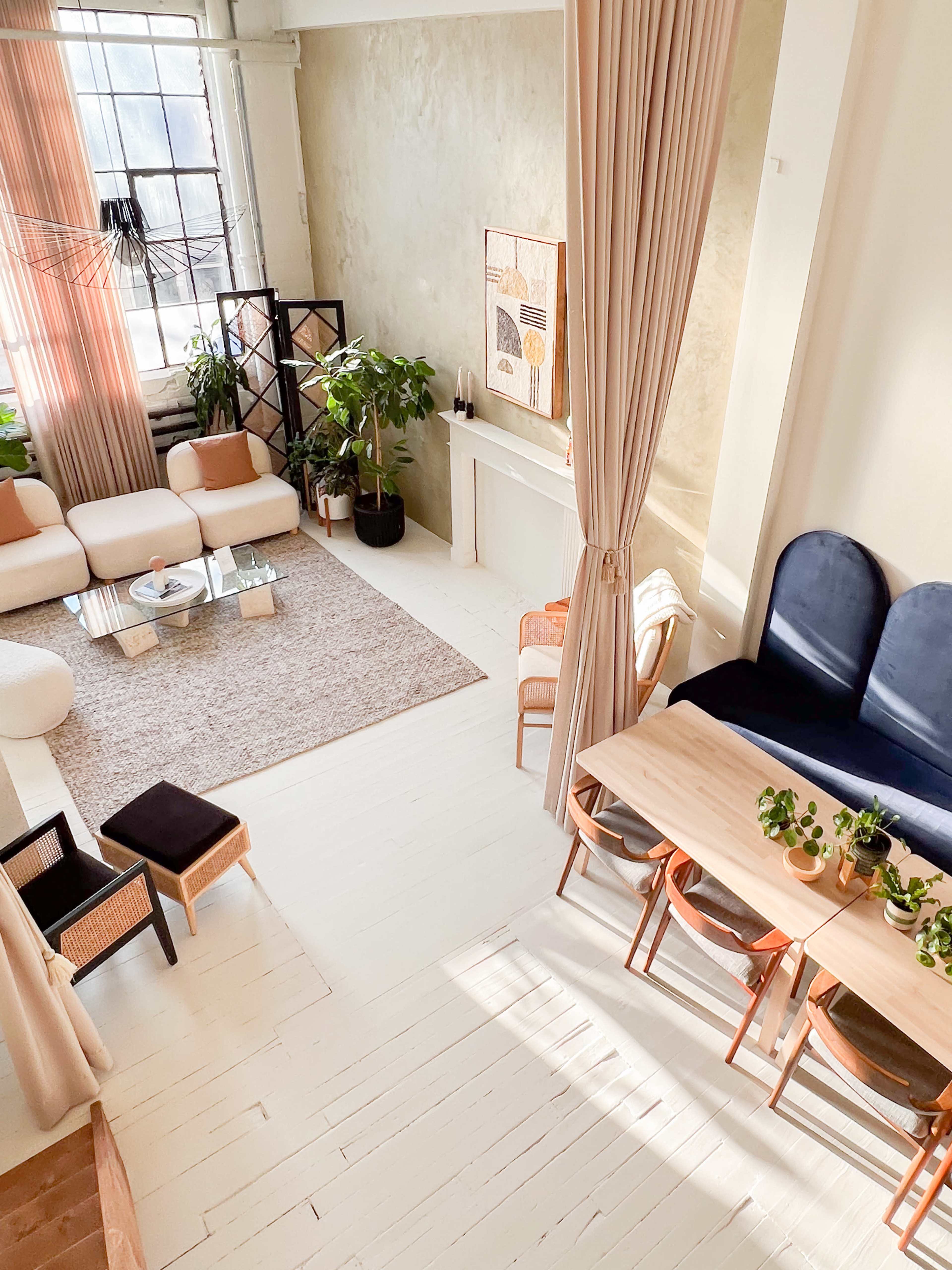 A spacious, well-lit room with modern furniture, including a sectional sofa, a dining table, and various plants.