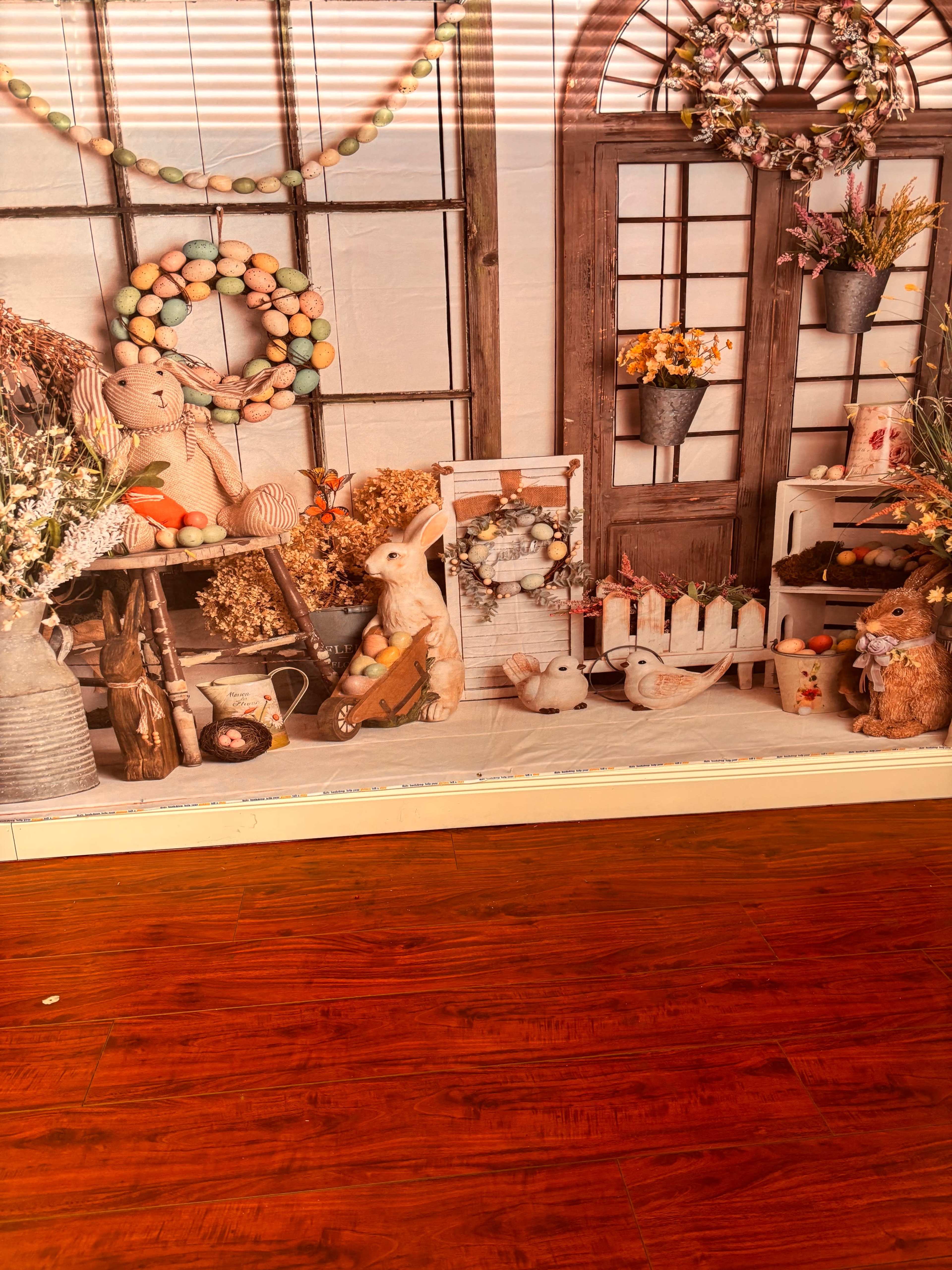 The image features a decorative display with bunnies, floral arrangements, and Easter-themed items set against a backdrop of windows.