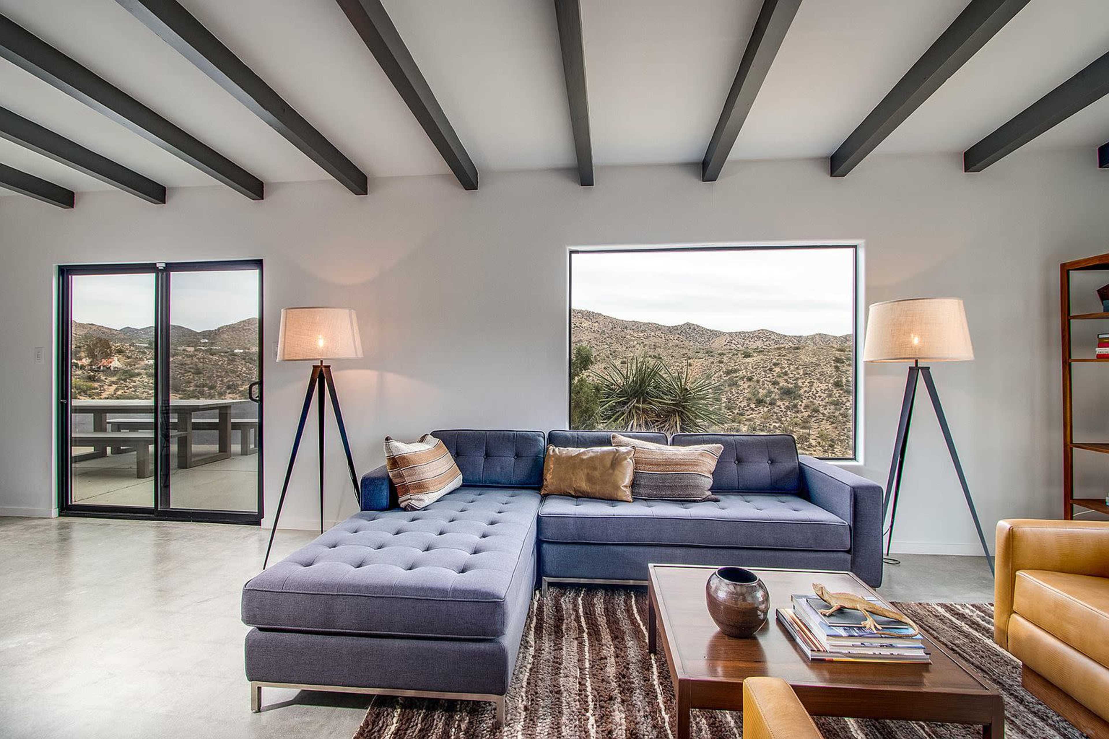 A modern living room features a blue sectional sofa, a wood coffee table, and large windows overlooking desert mountains.