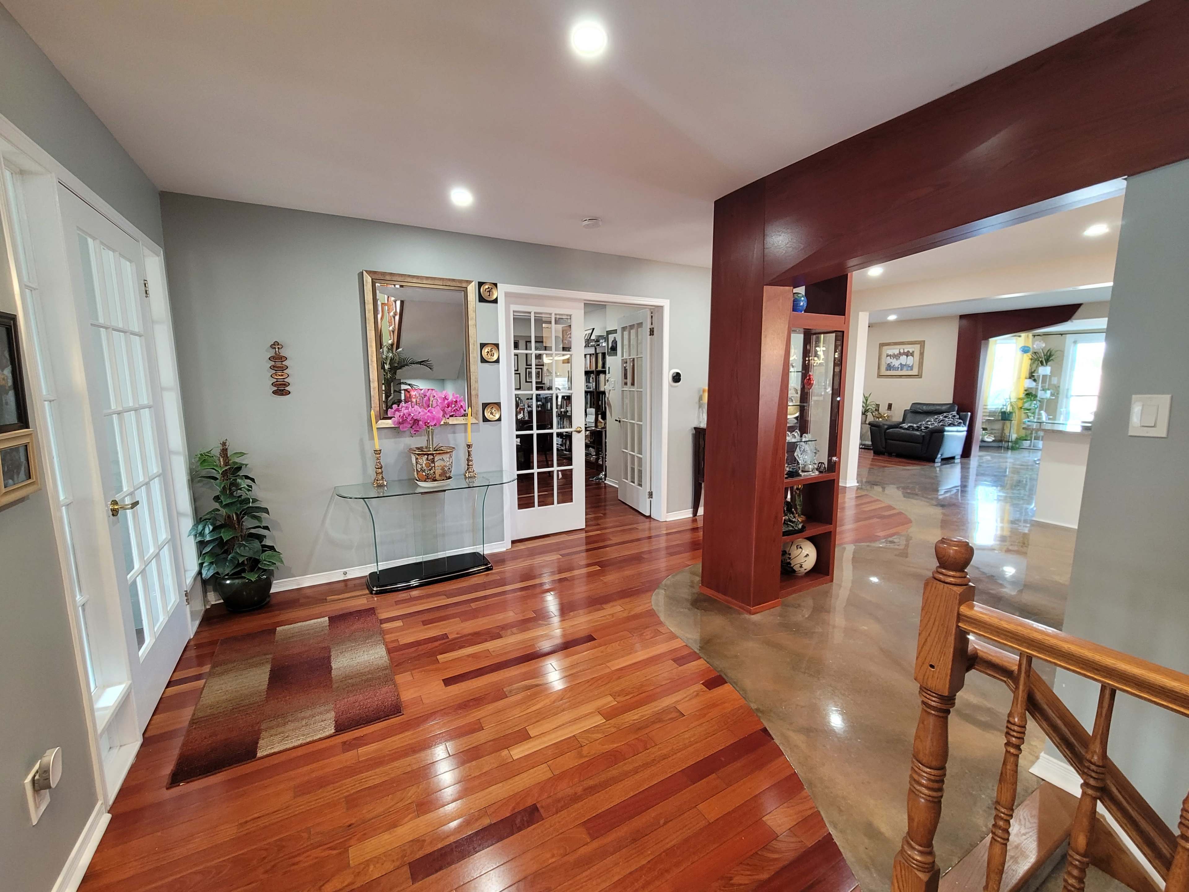 A well-lit entrance hall with hardwood flooring, a glass console table, and French doors leading into another room.