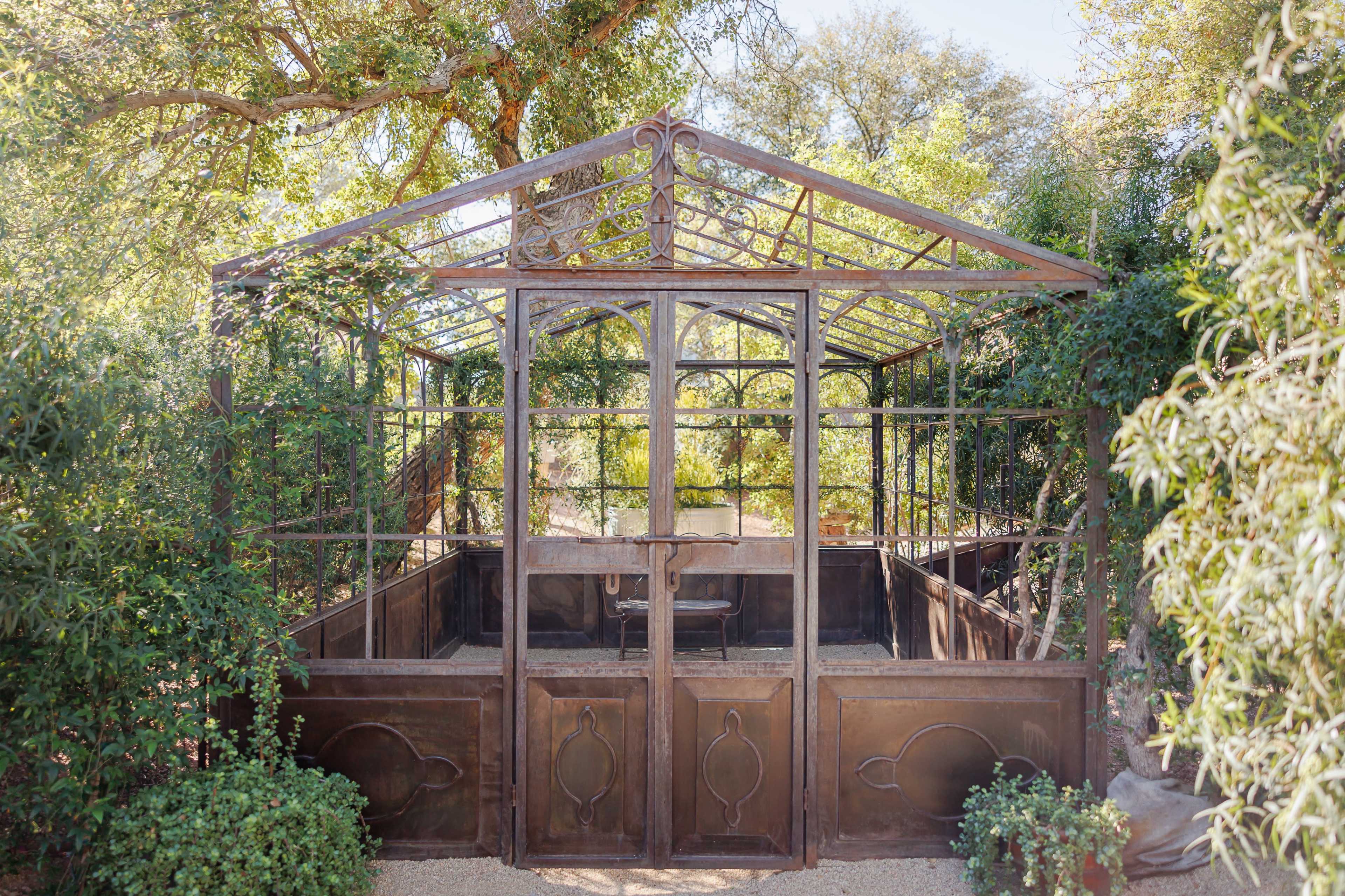 The image shows a glass-paneled greenhouse surrounded by greenery and trees.