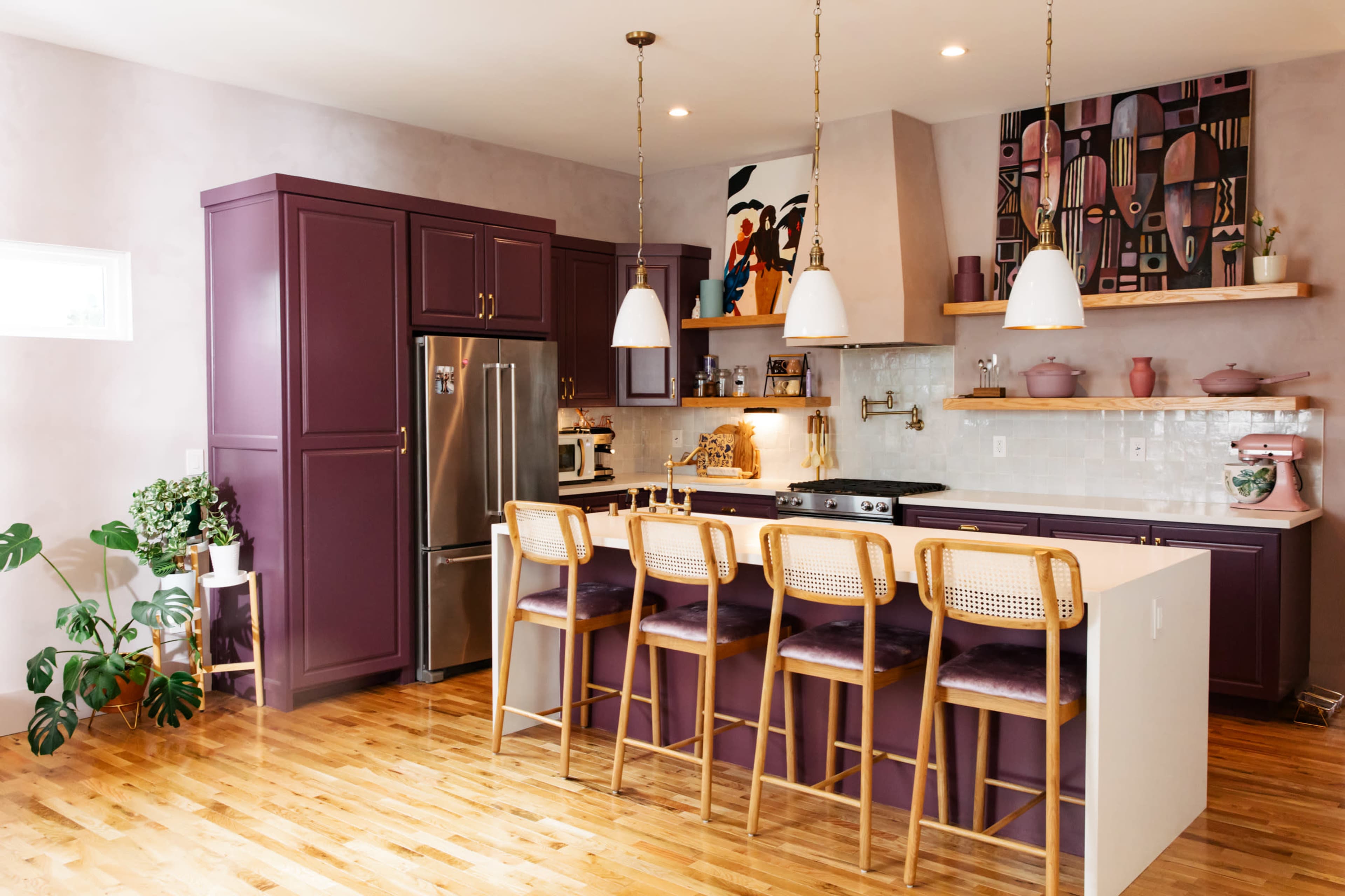 A modern kitchen features purple cabinetry, a spacious island with bar stools, and decorative wall art.