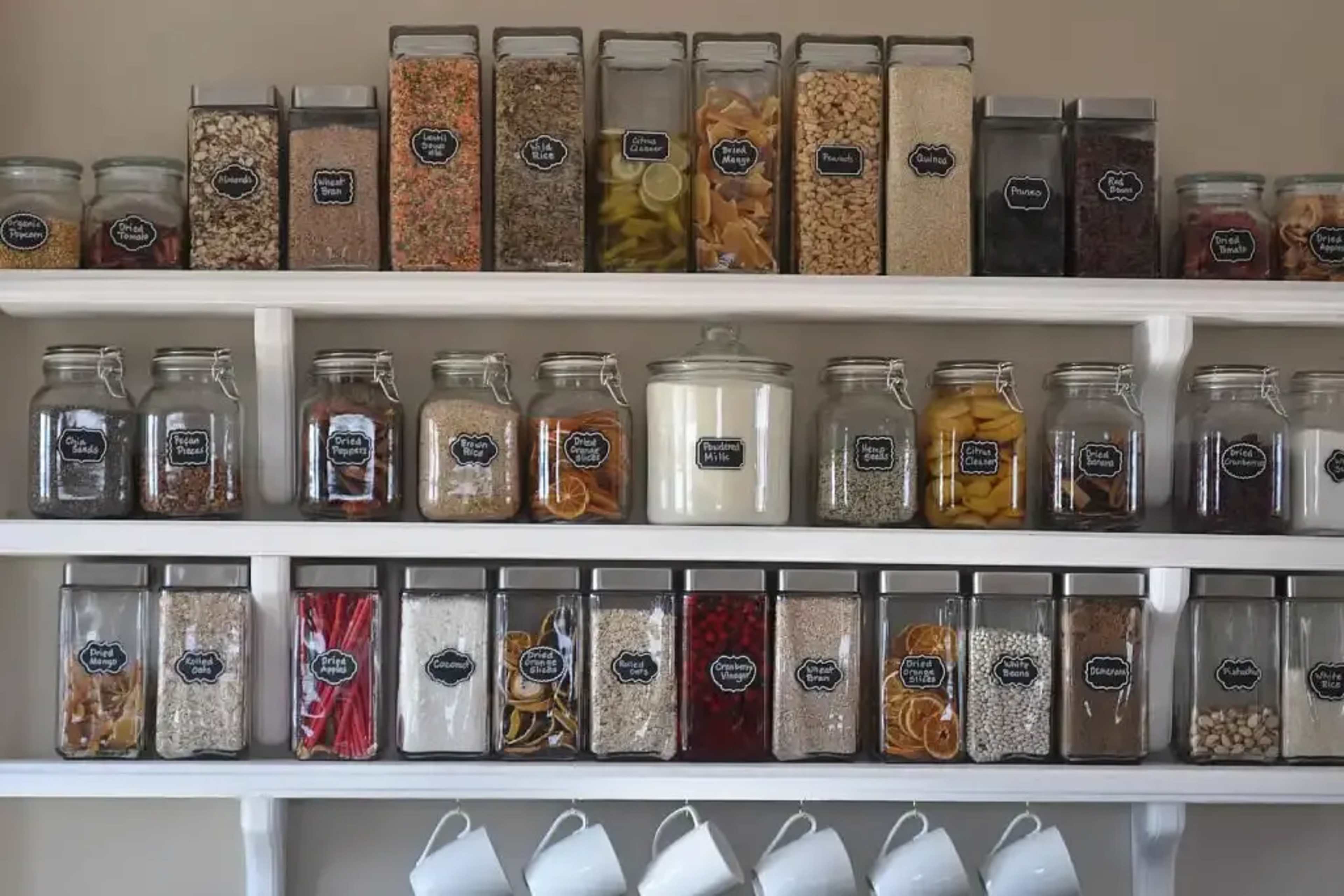 A neatly organized shelf displays a variety of labeled glass jars filled with grains, dried fruits, and spices.