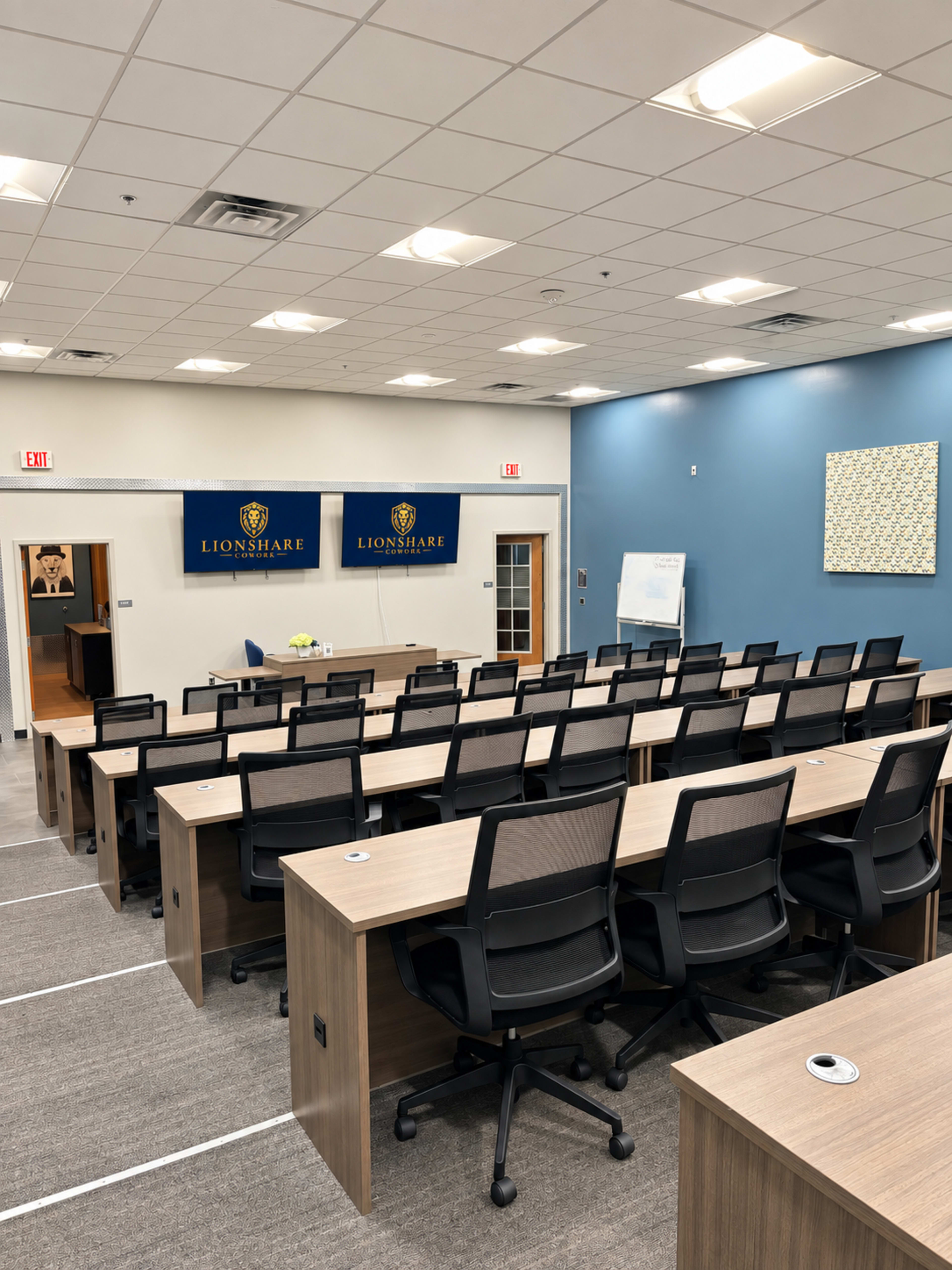 The image shows a modern classroom or meeting space arranged with rows of desks and chairs, featuring a projection screen and a blue accent wall.