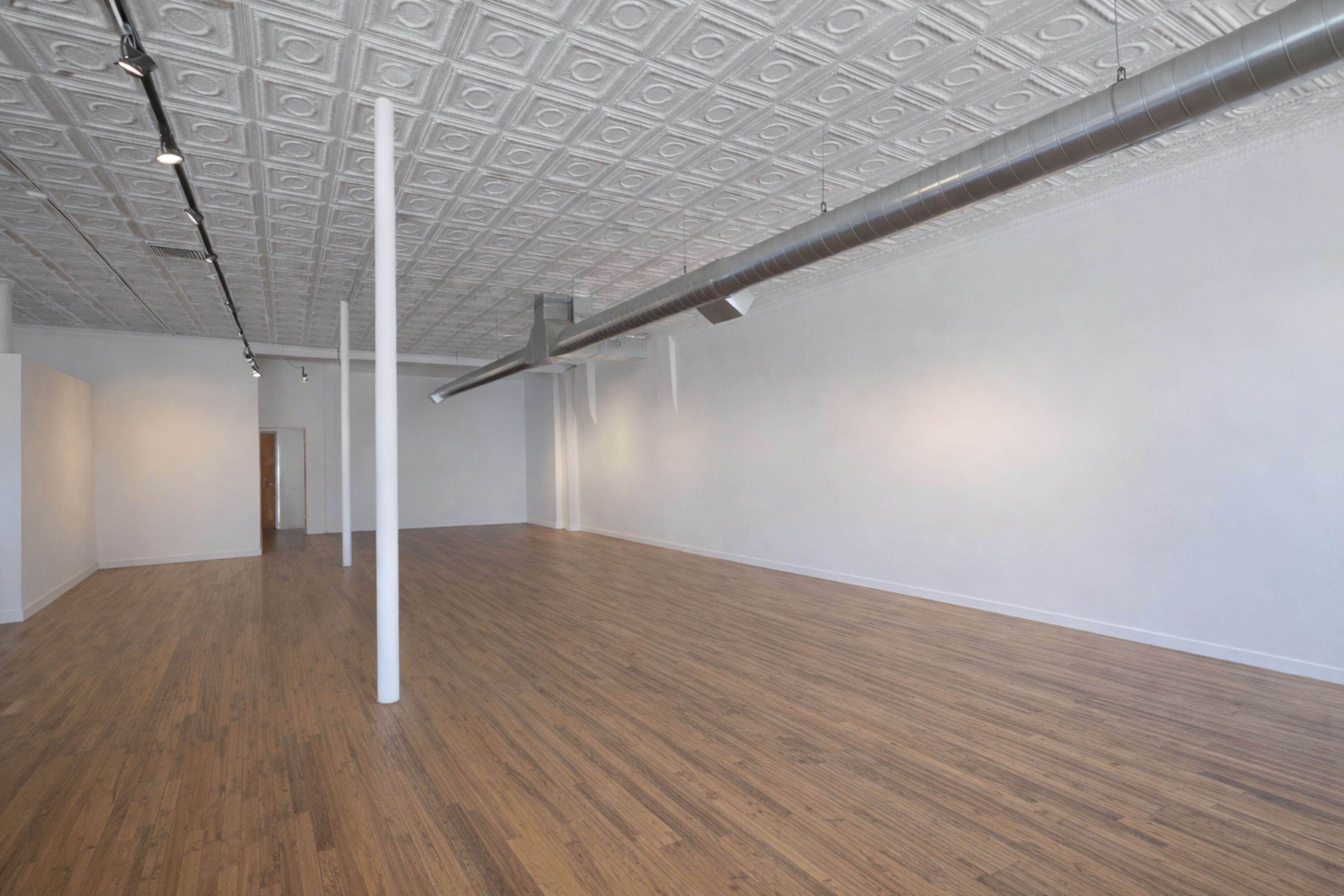 The image shows an empty art gallery with a wooden floor, white walls, and a decorative ceiling.