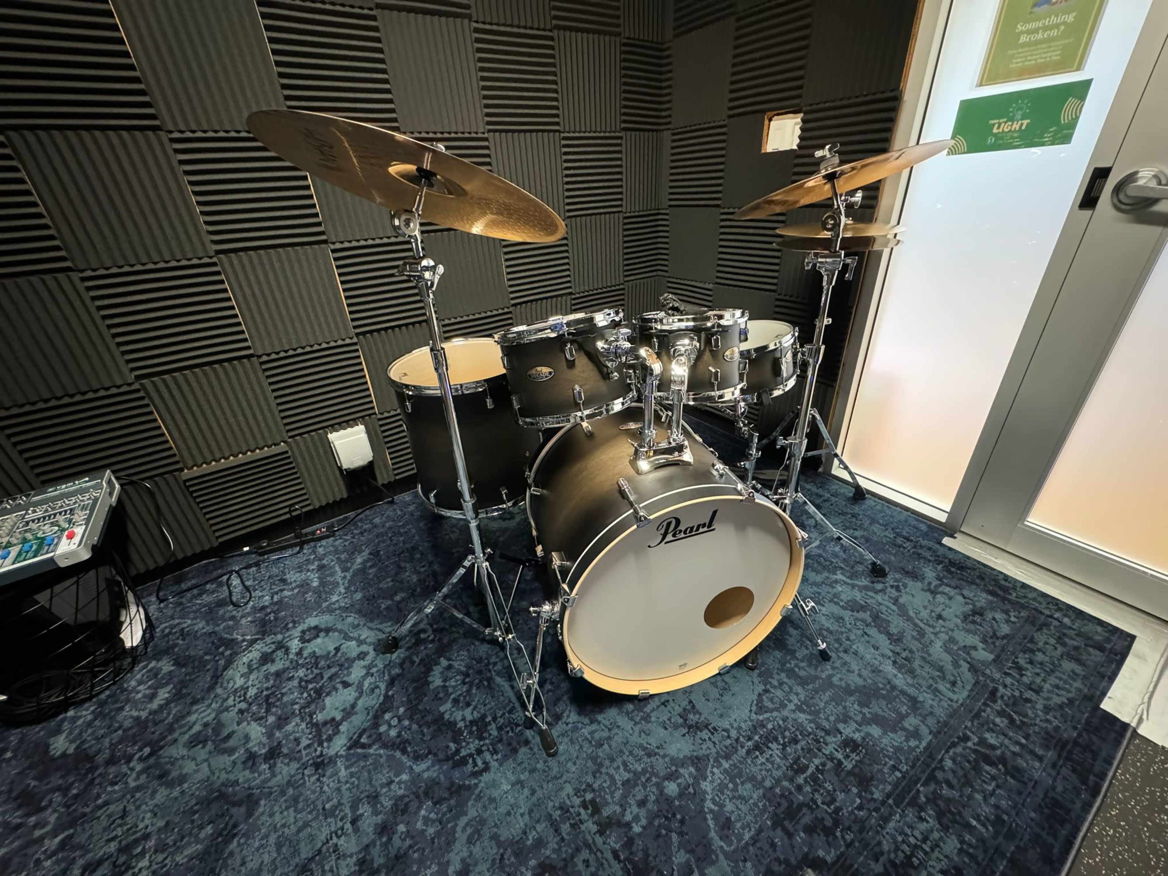 A Pearl drum kit is set up in a soundproofed room with acoustic paneling and a door leading to the outside.