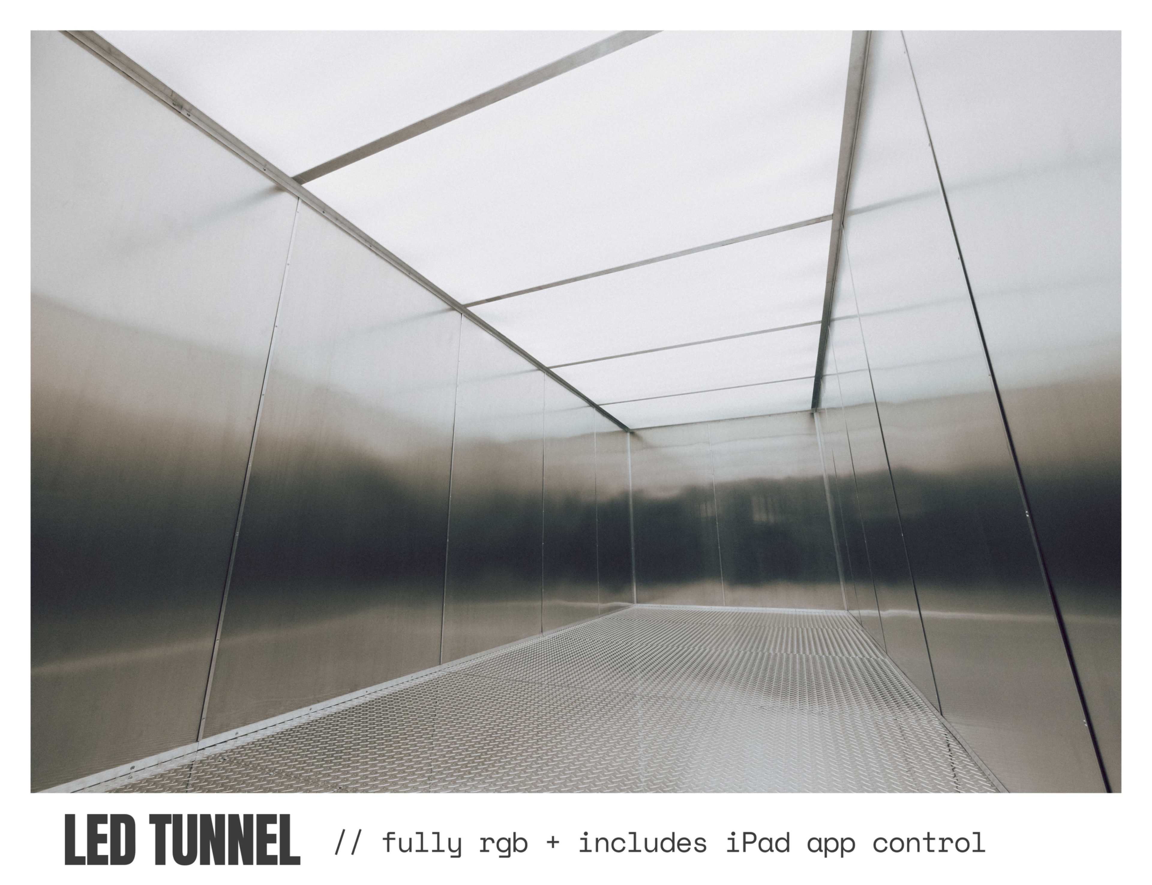 The image shows the interior of a metallic tunnel with smooth surfaces and LED lighting, featuring a grated floor.