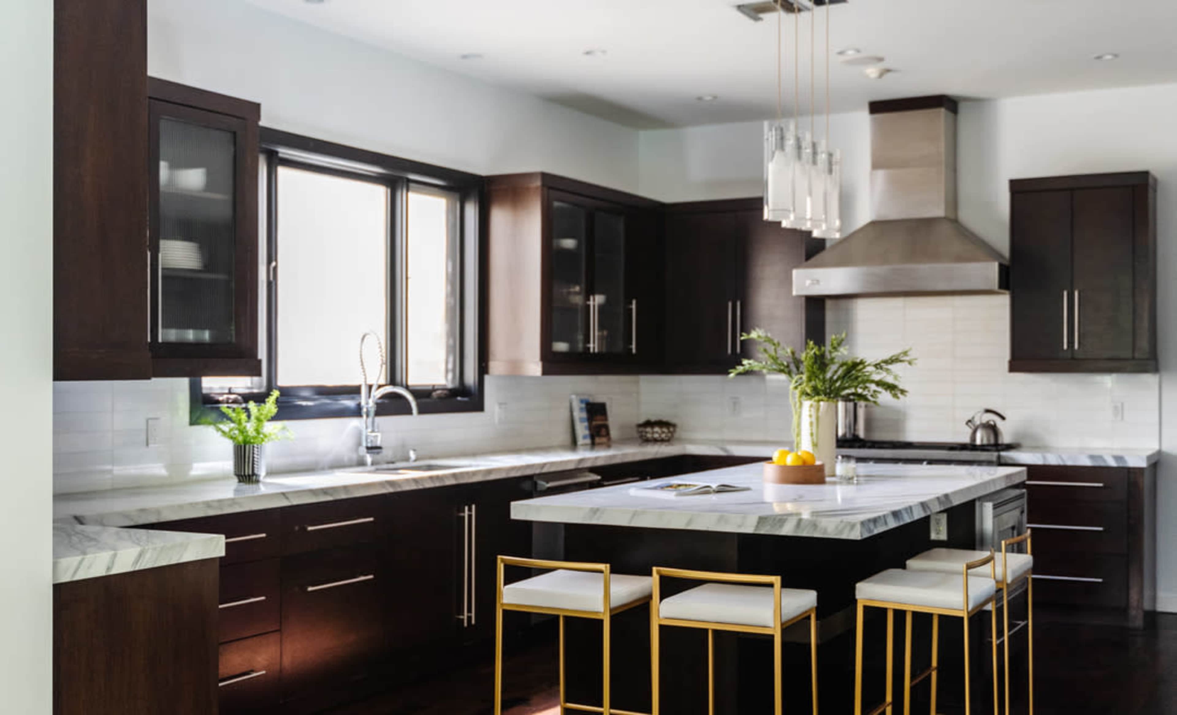 A modern kitchen features dark wood cabinets, a marble countertop island with gold bar stools, and stainless steel appliances.