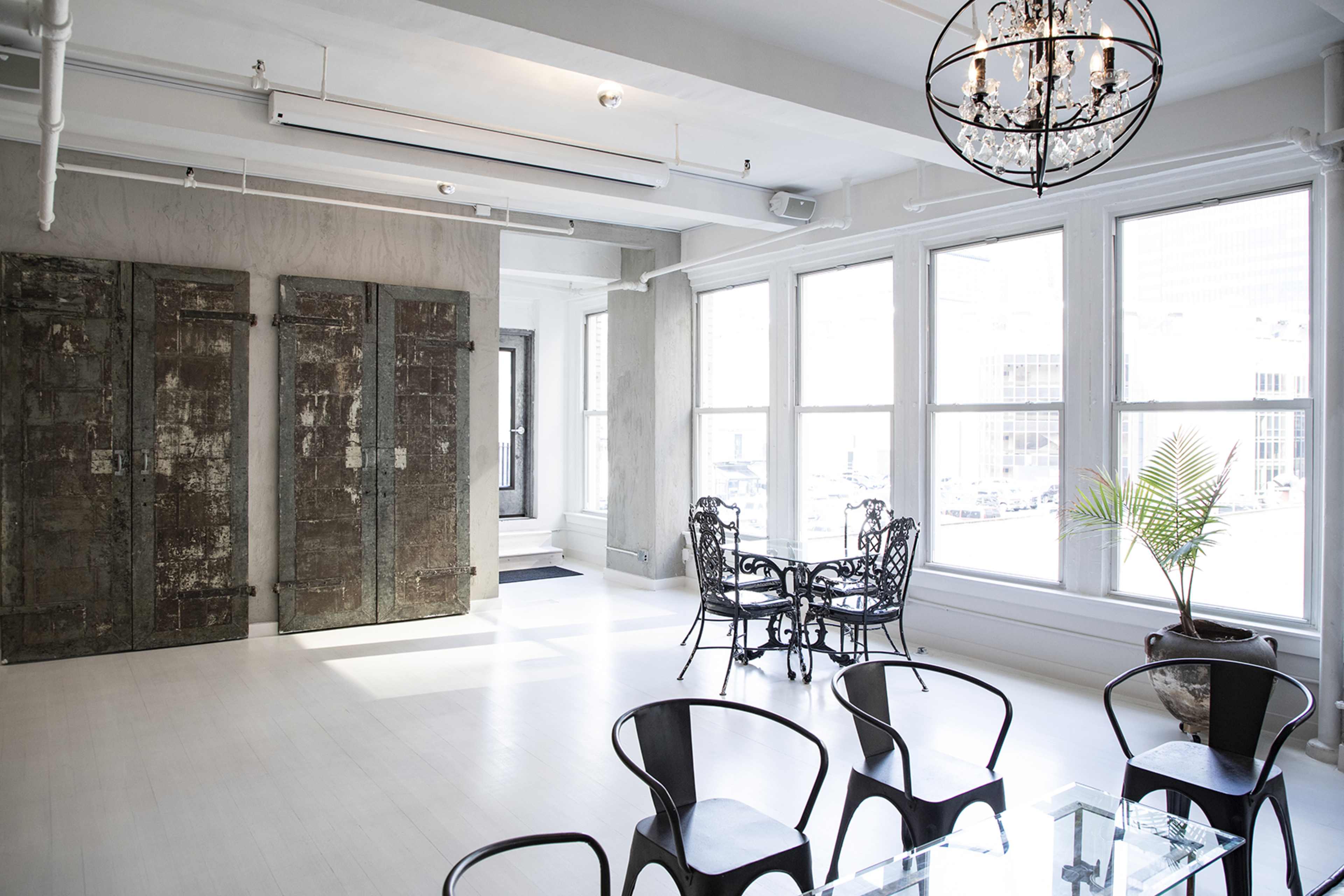 A bright room with large windows, a glass table, black chairs, and two vintage doors mounted on the wall.