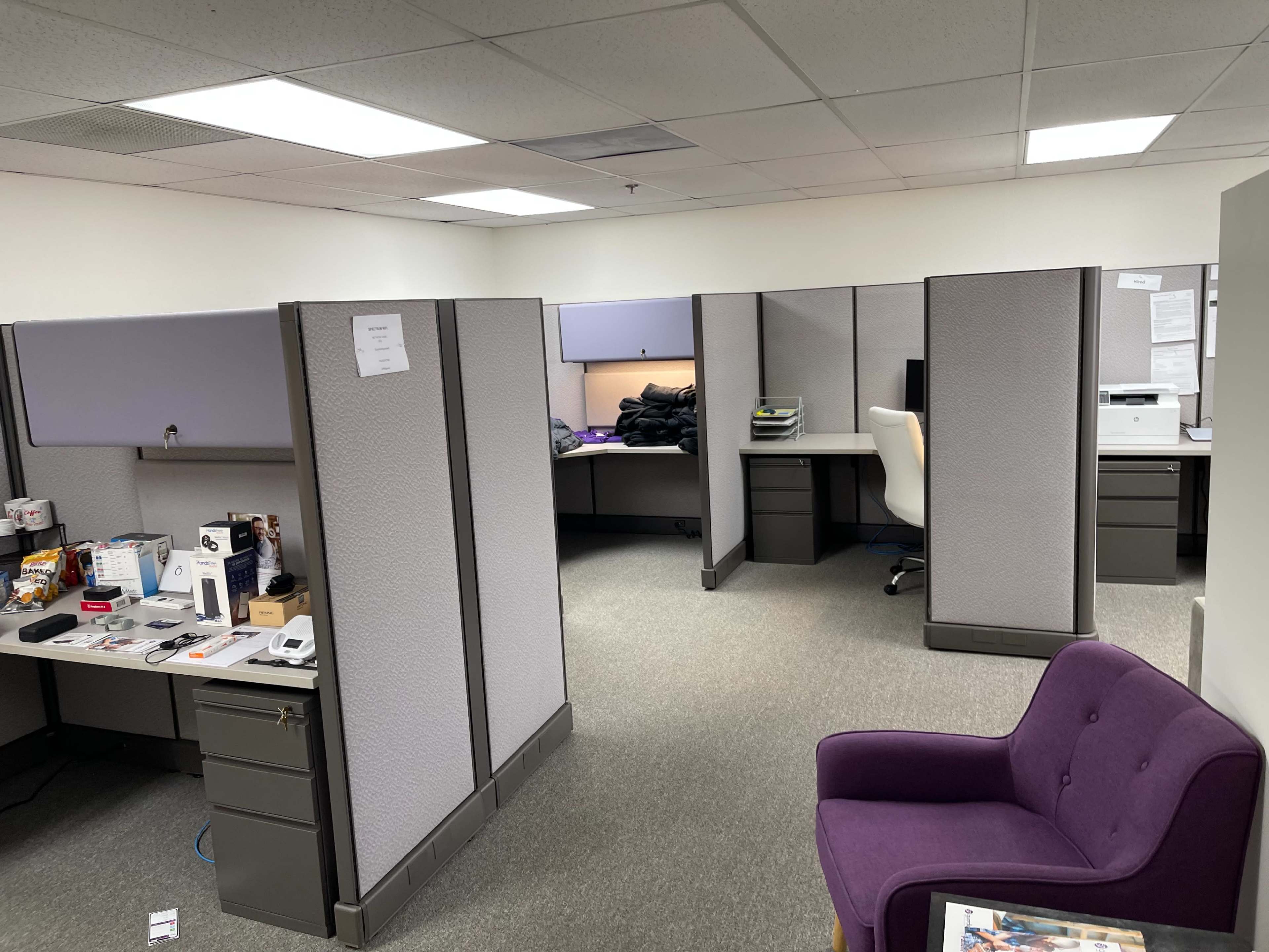 An office cubicle layout with several workstations, including a chair and a purple armchair in the corner.