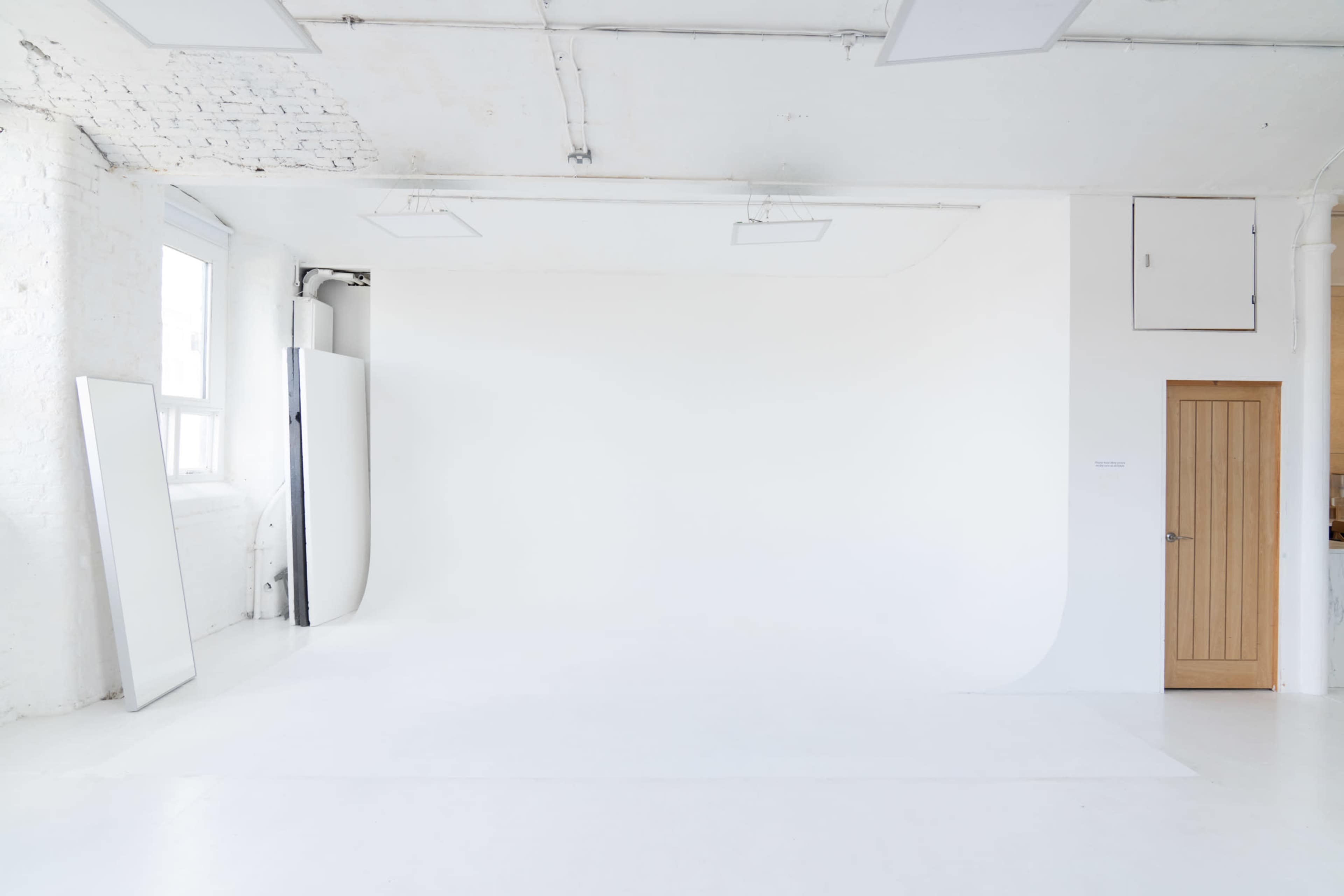 A spacious, empty studio with a seamless white backdrop, white floors, and minimal furnishings.