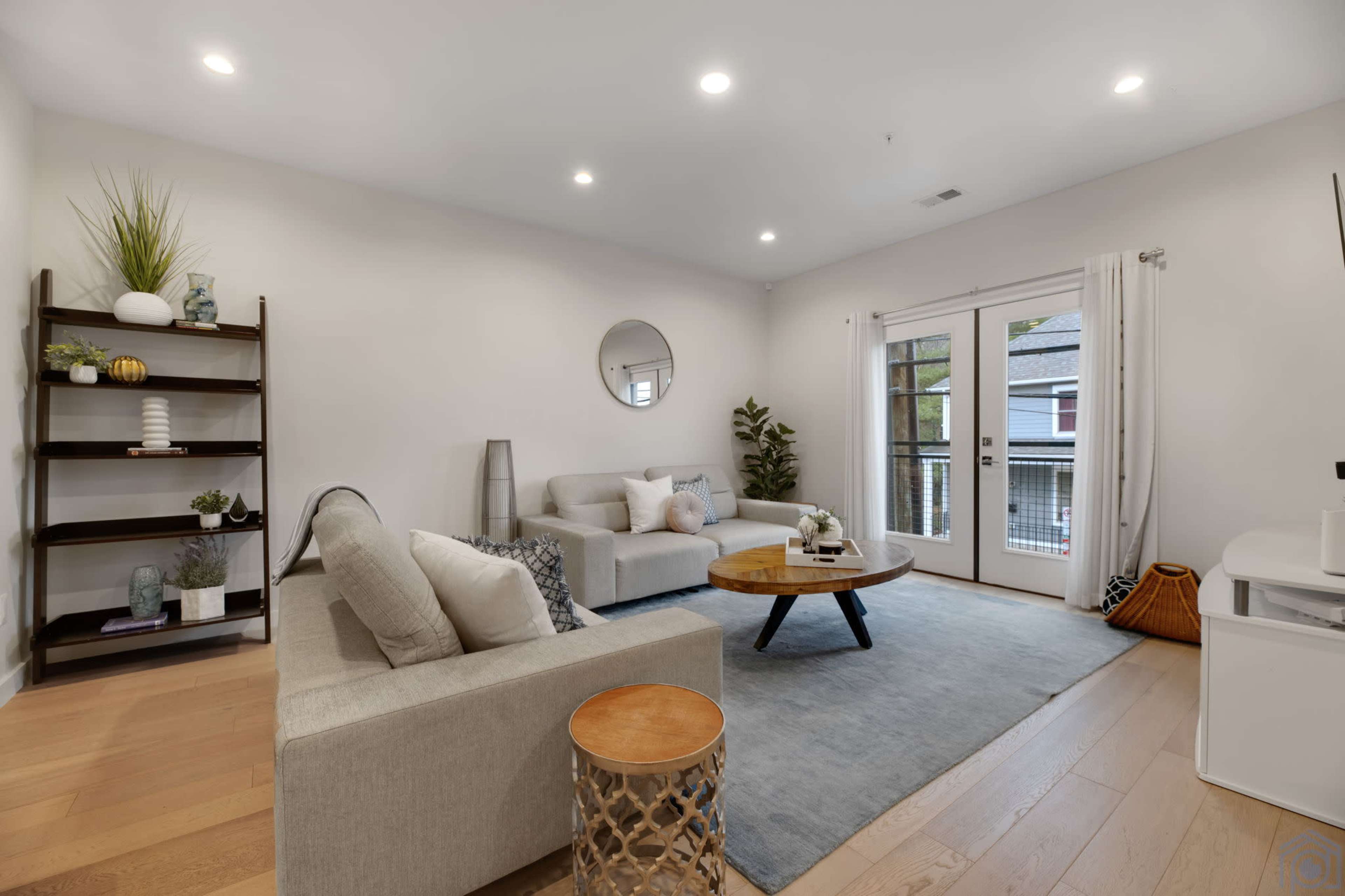 A modern living room featuring a light-colored sofa, a round coffee table, and a bookshelf, with large windows that lead to an outdoor area.