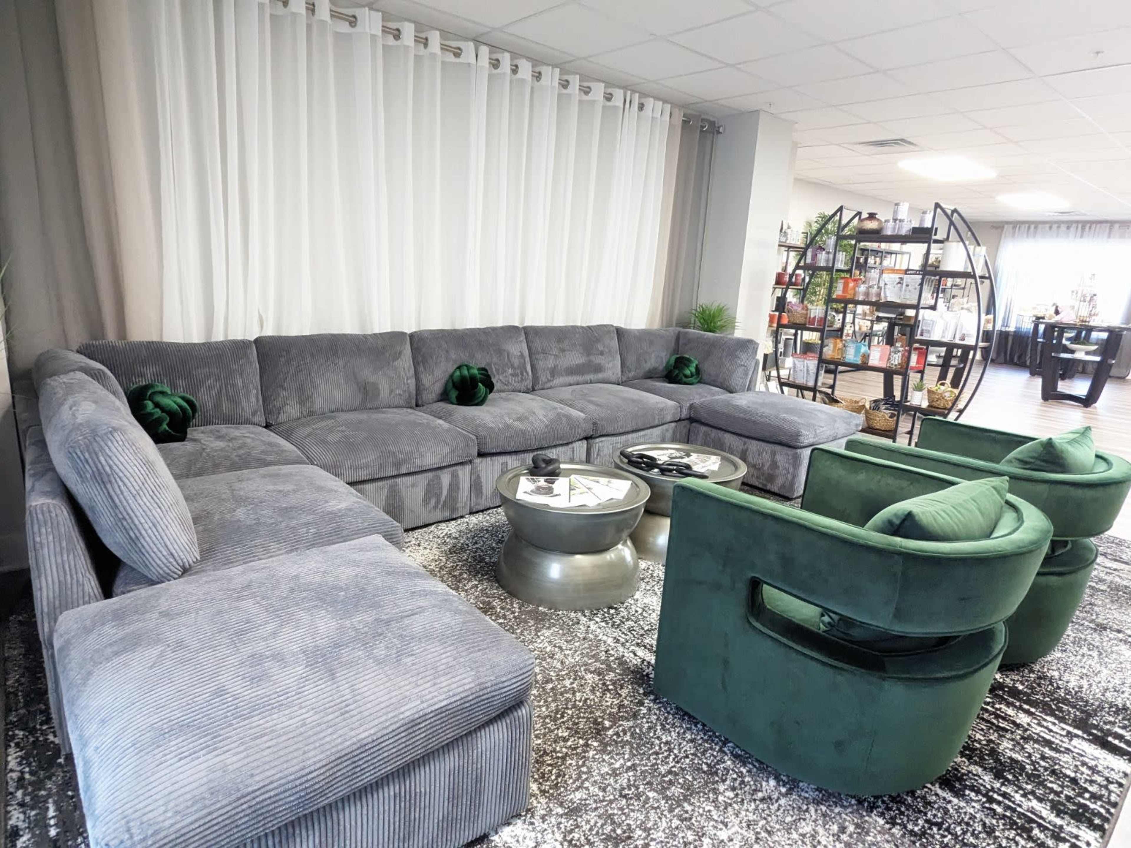 A modern living room setup with a large gray sectional sofa, two green chairs, and a round glass table on a textured rug.