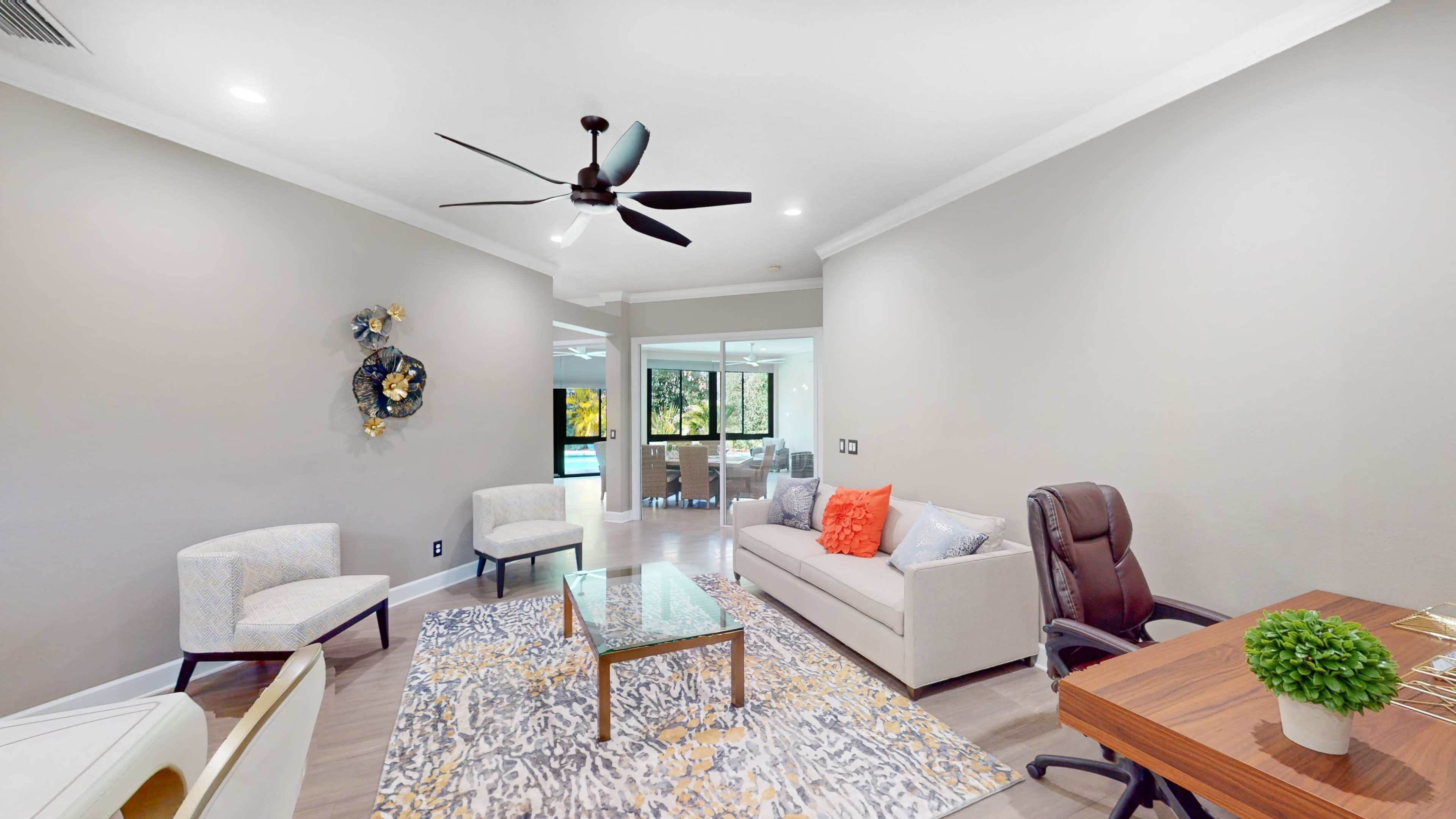 The living area features a sofa, two chairs, a glass coffee table on a patterned rug, and a ceiling fan.