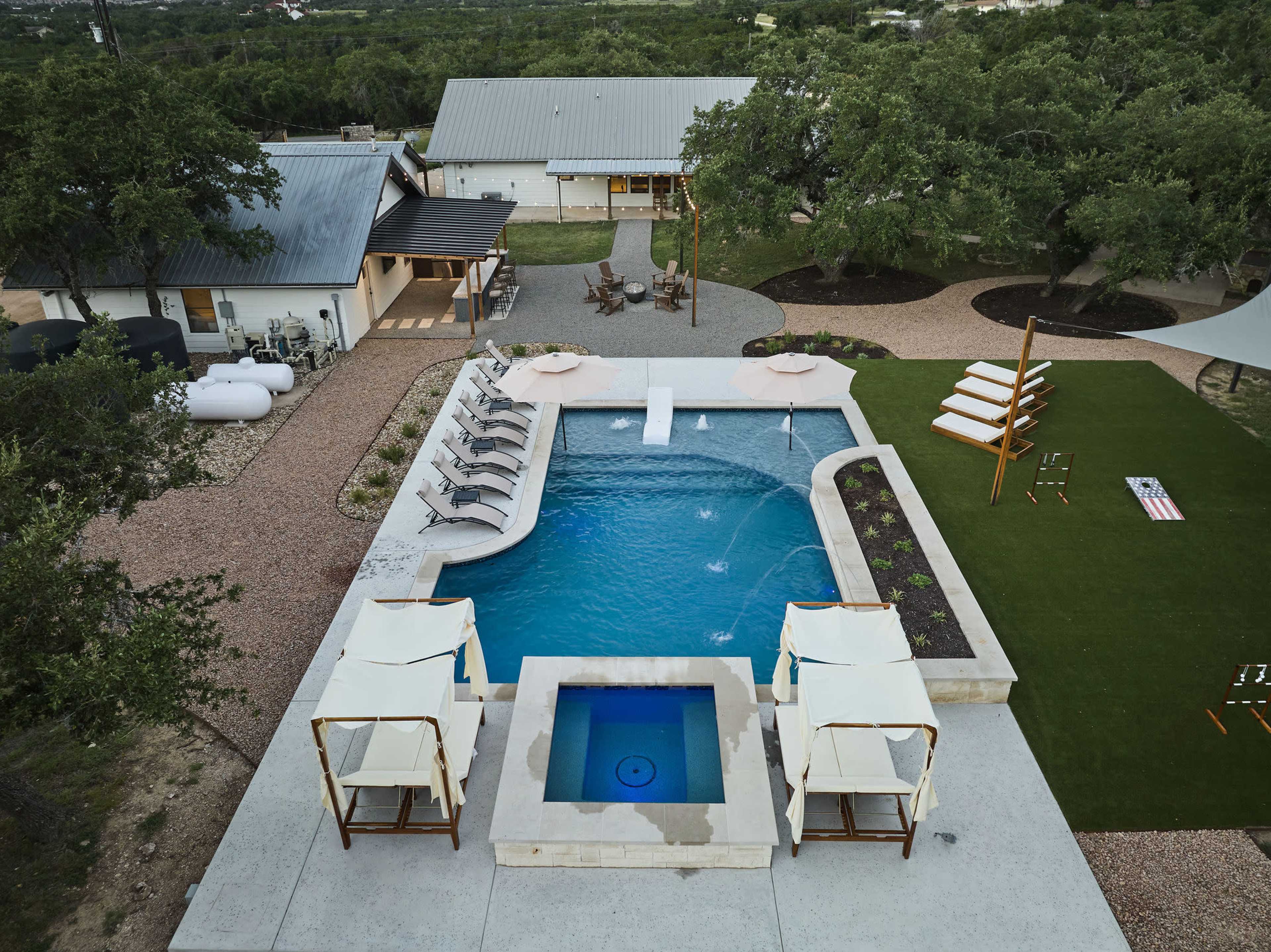 The image shows a well-designed outdoor area featuring a swimming pool, spa, lounge chairs, and nearby landscaping with trees and a seating area.