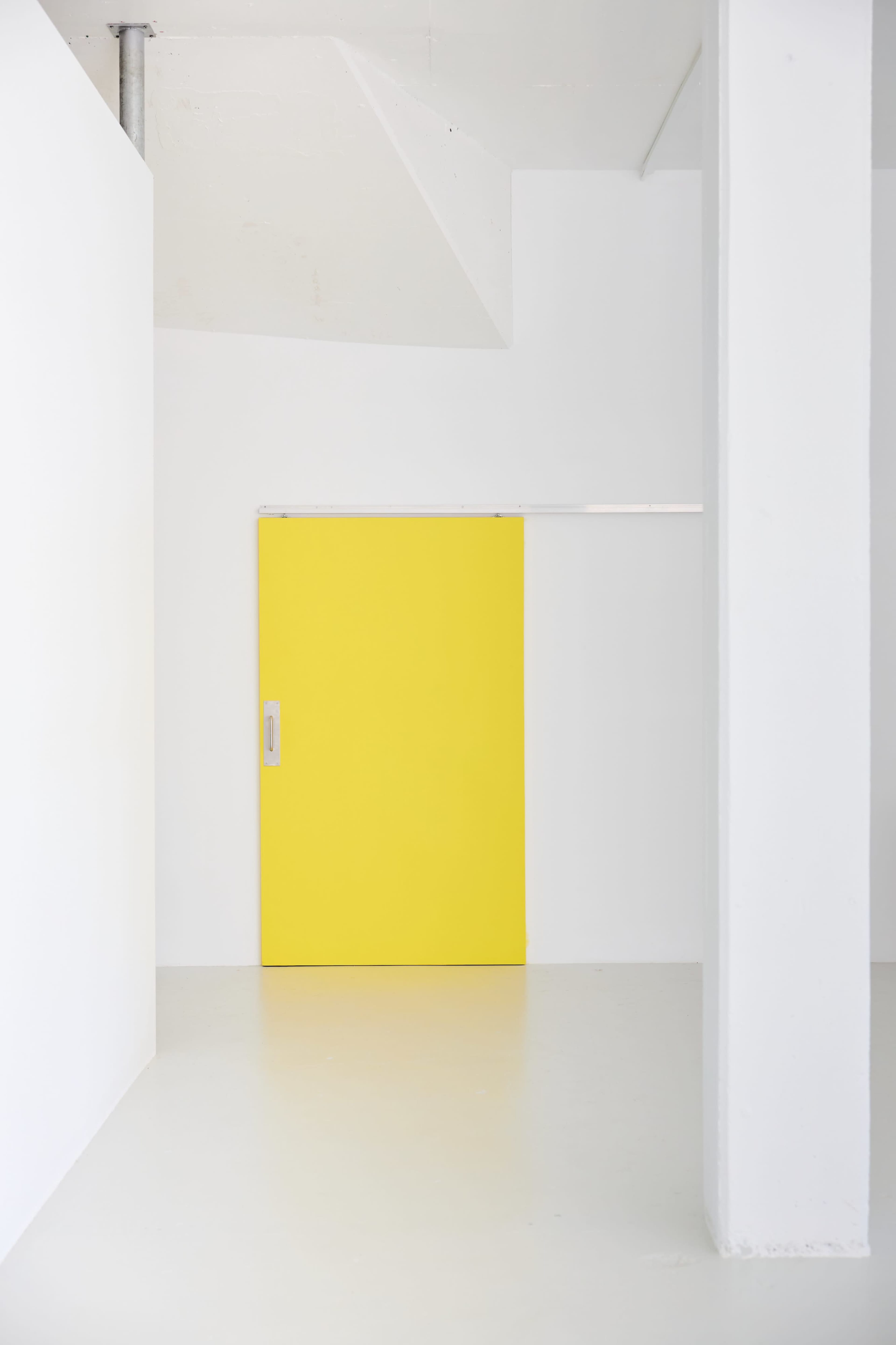 A bright yellow sliding door is centered in a minimalist white room with smooth floors and large white walls.