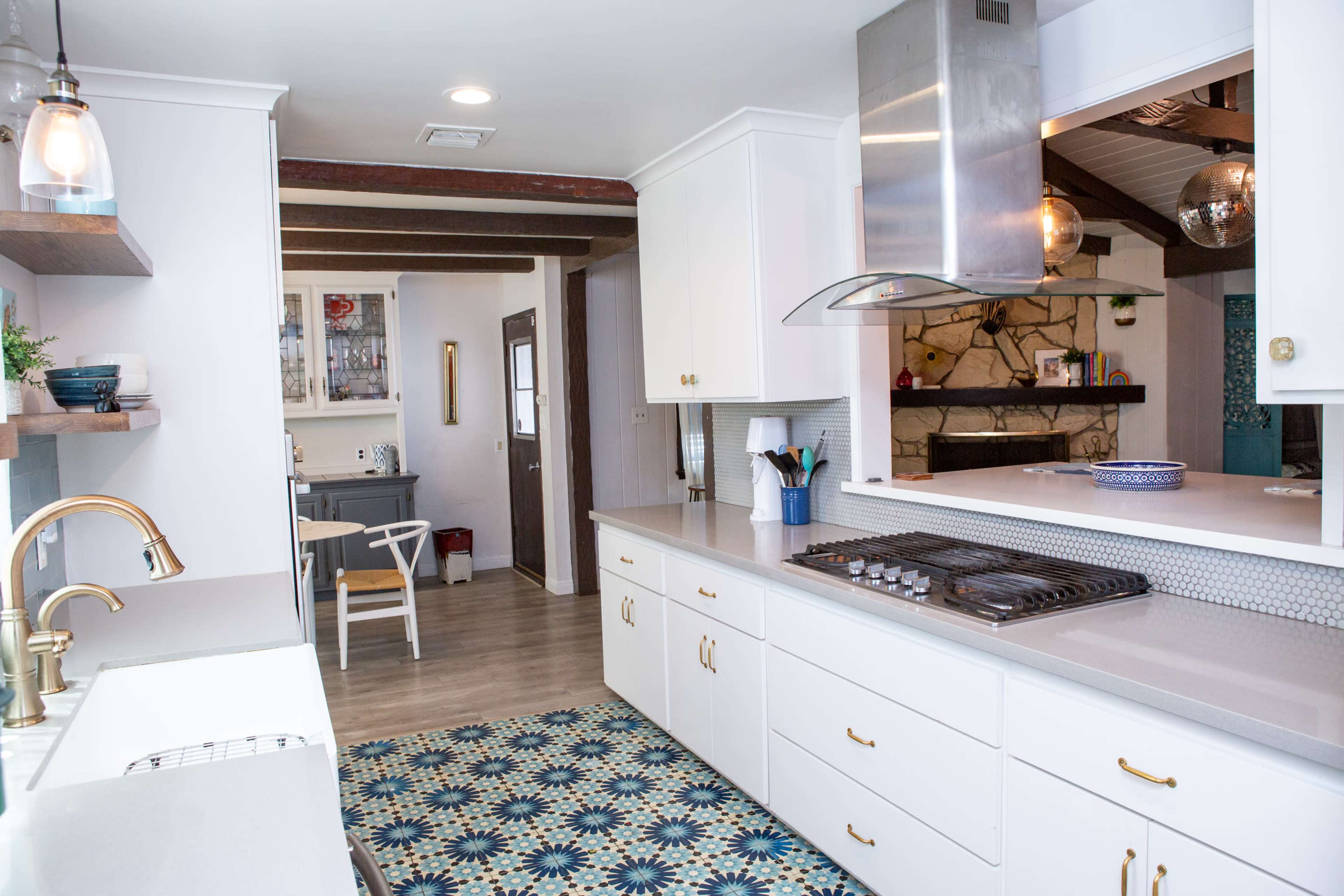 A modern kitchen with white cabinets, a gas stove, and a patterned rug, leading to an adjoining dining area.