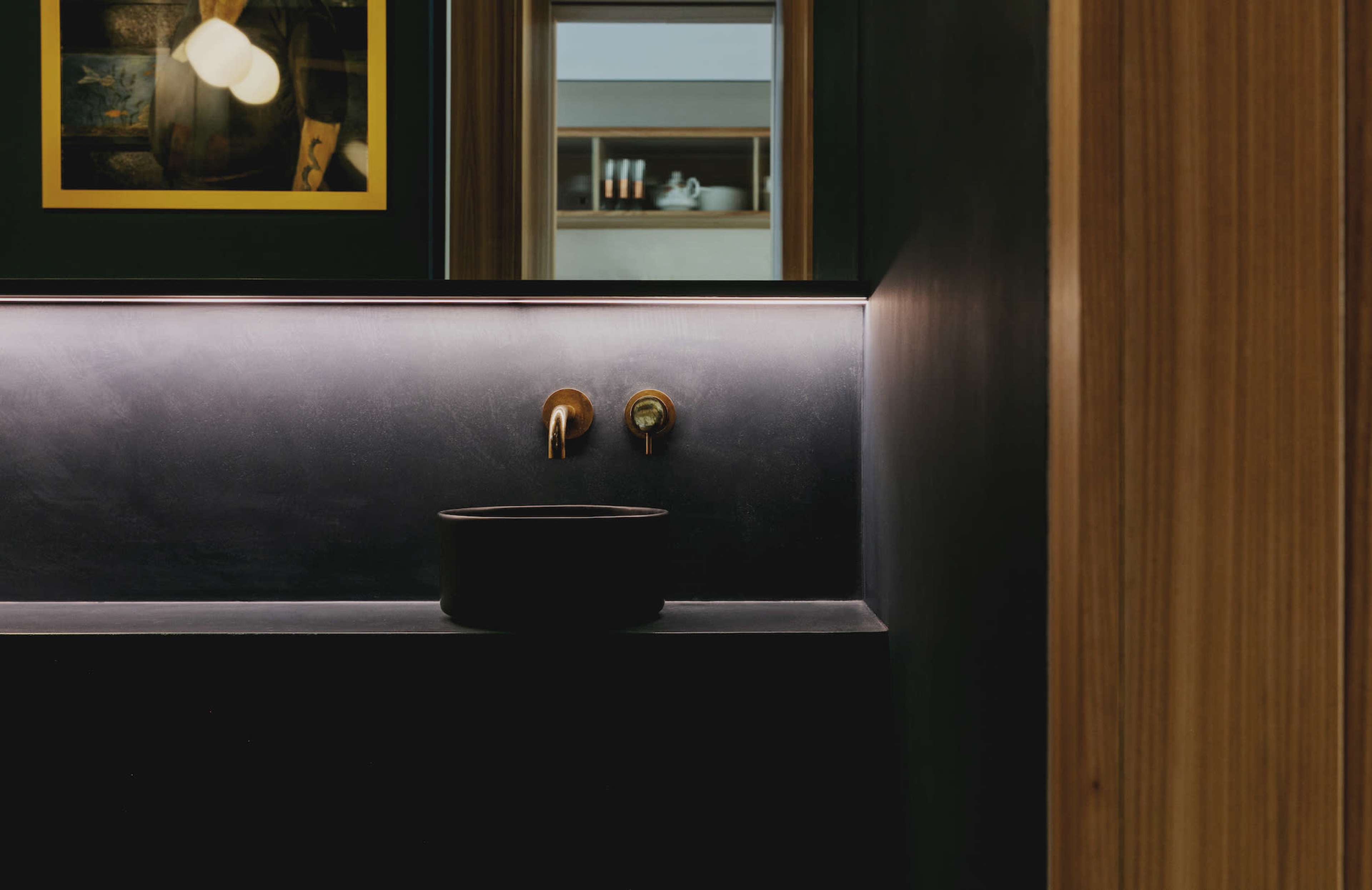 A sink with two taps set against a dark wall, illuminated by a strip of indirect lighting.