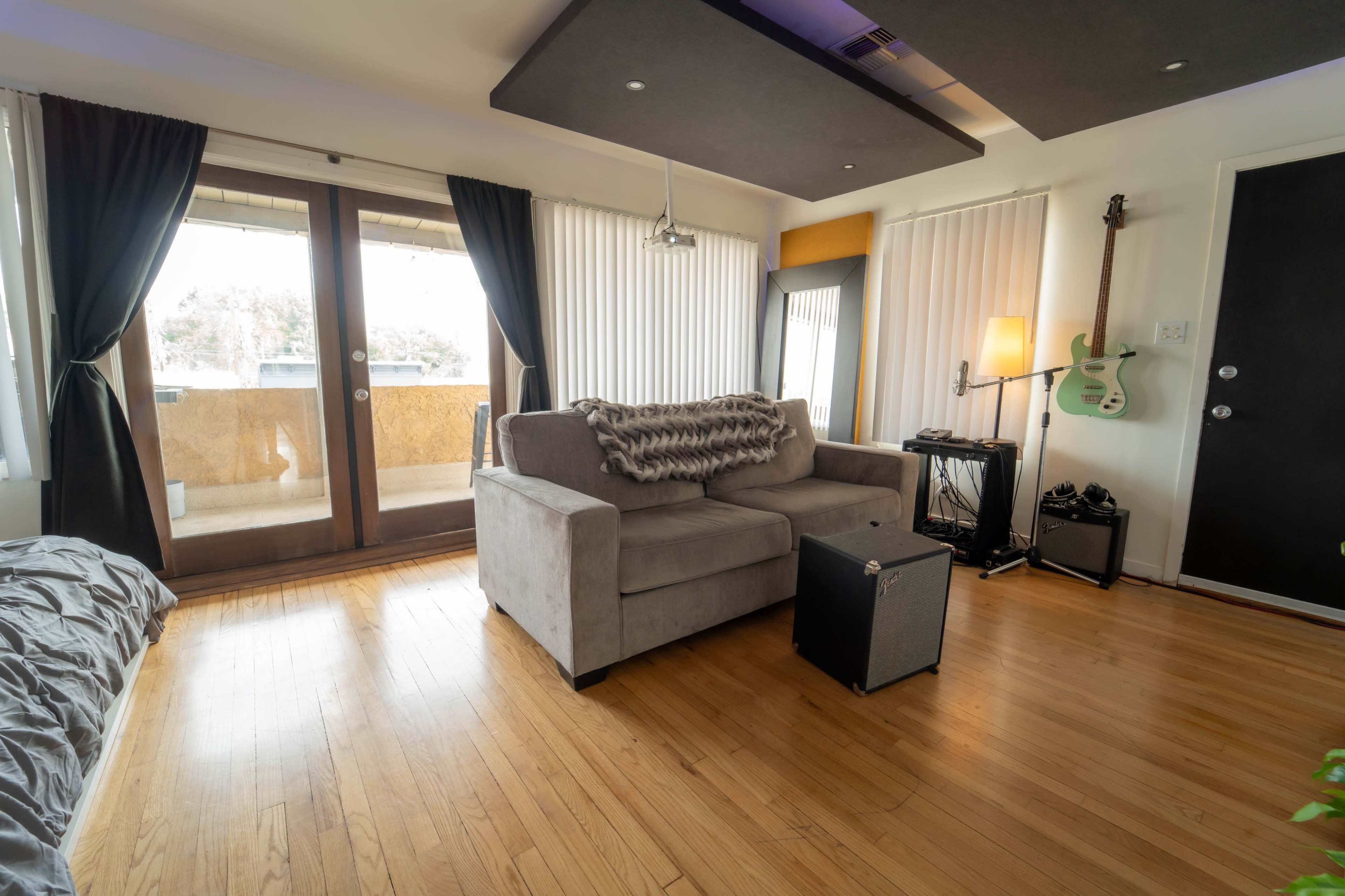 A cozy living room featuring a gray couch, a coffee table, and a balcony view through sliding glass doors, with musical instruments placed nearby.