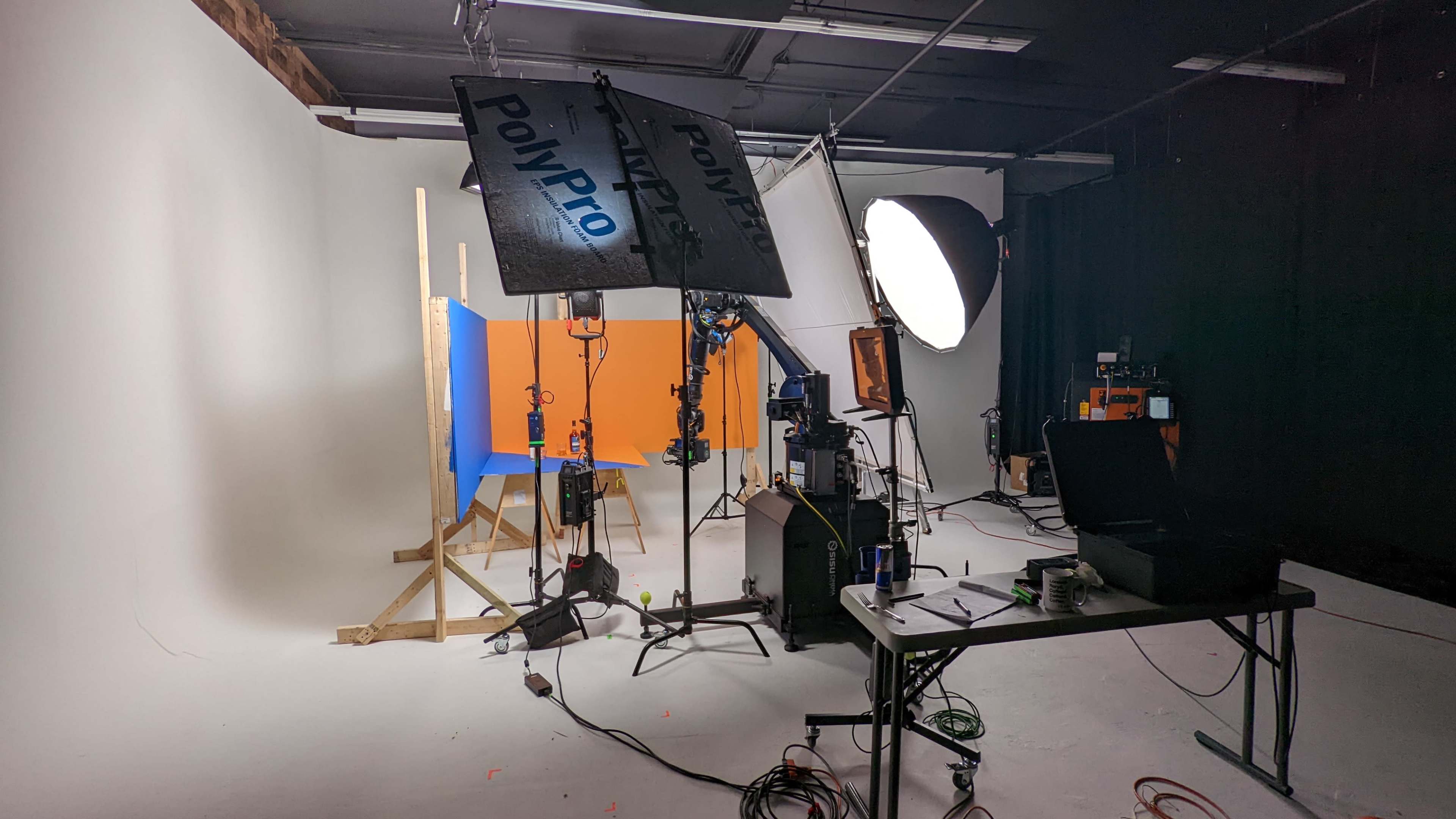 A photography studio setup with lighting equipment, a blue and orange backdrop, and various cameras and accessories on a table.
